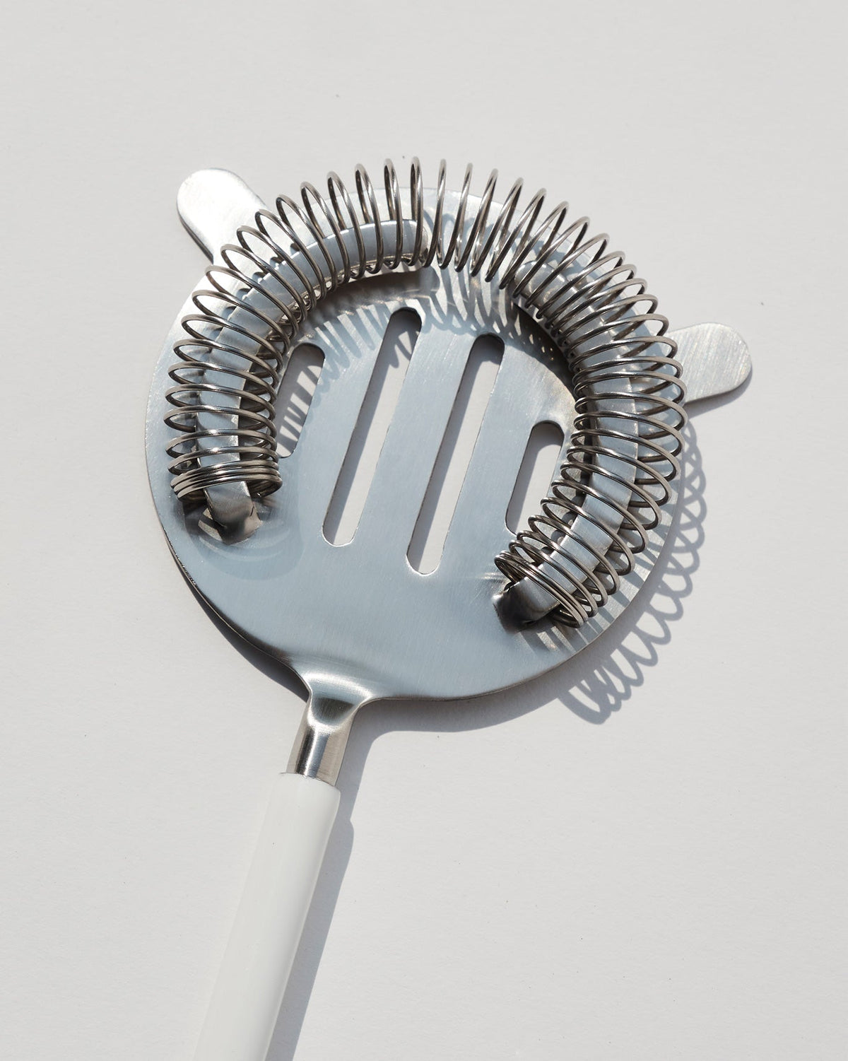 Close-up of Riverside Cocktail Strainer -White showing its coiled rim and slotted head.