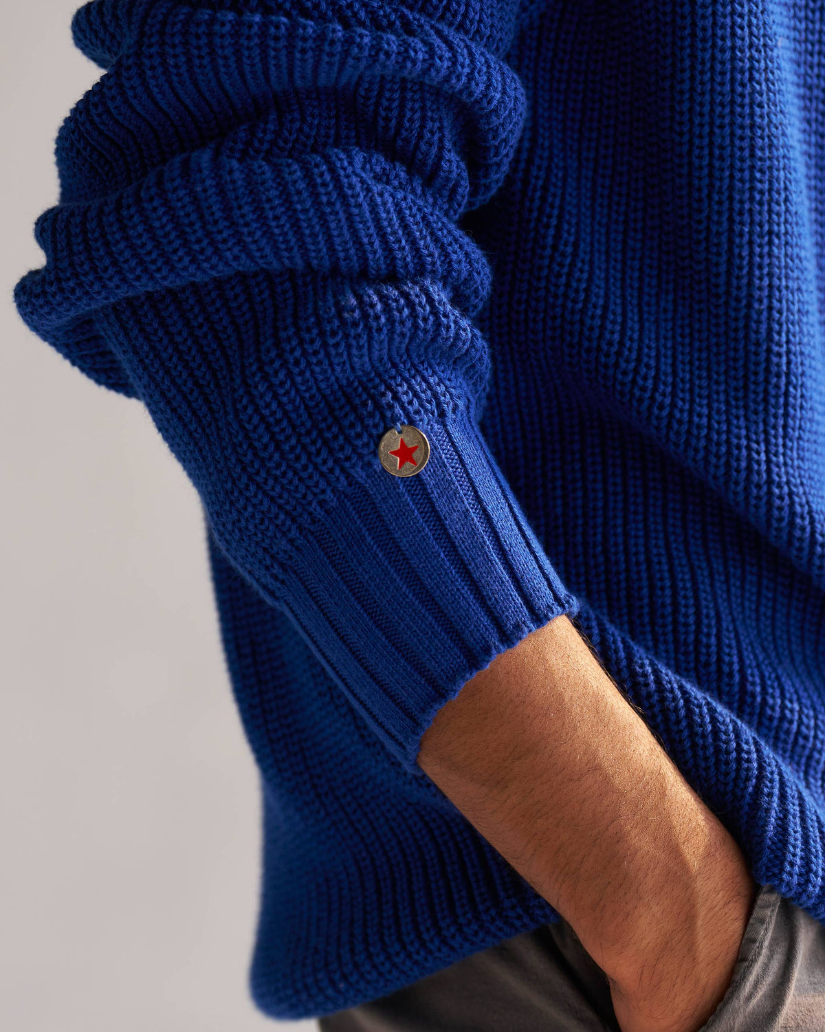 Close-up of a blue Coast sweater sleeve with a red star button at the cuff.