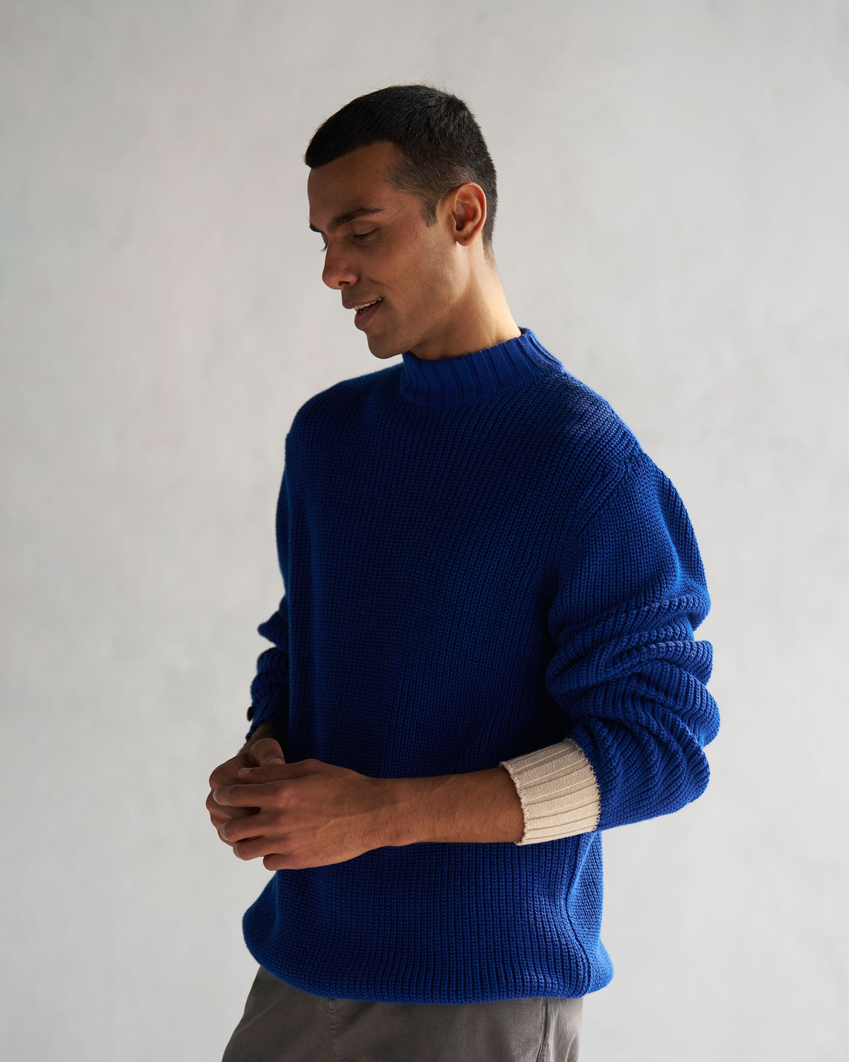 Person wearing a blue Coast sweater, looking down with hands at the waist.