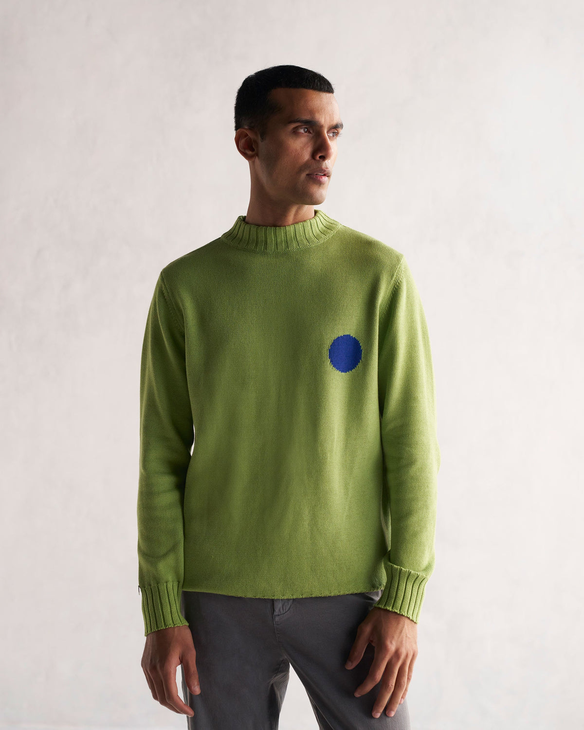 Person in a green knit Coast Crew-Neck Sweater with a blue circle on the chest.
