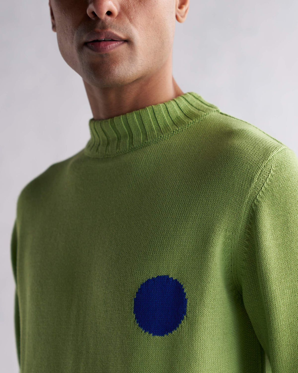 Close-up of green Coast Crew-Neck Sweater showing a blue circle motif on the chest.