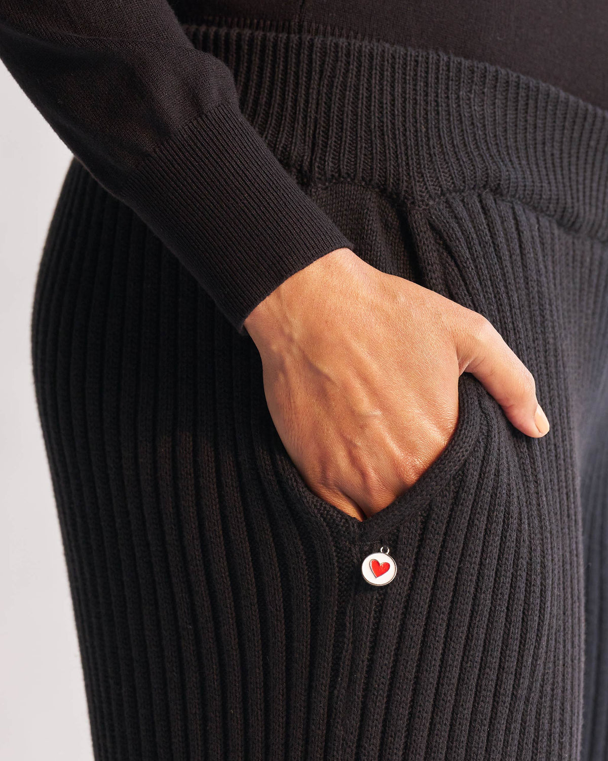 Close-up of black Ribbed Knit Trousers showing a side pocket and a small heart charm.