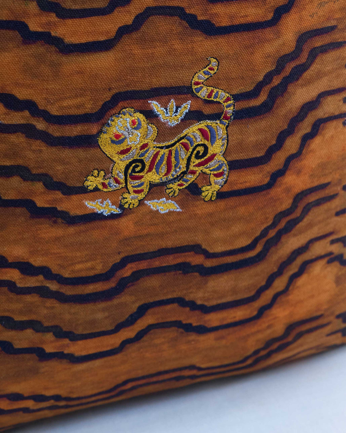 Close-up of Rajasri Cushion Cover showing a gold tiger motif on wavy stripes.