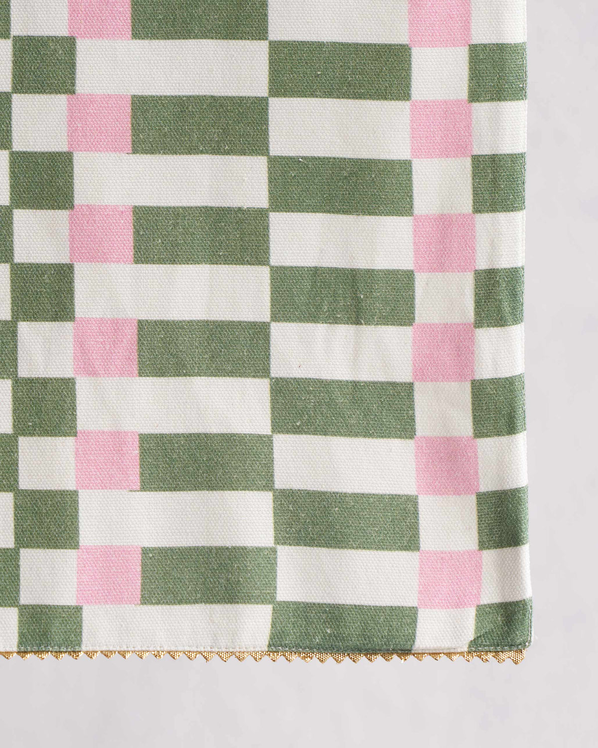 Close-up of plethora table runner showing its green and pink checks and gold edging.