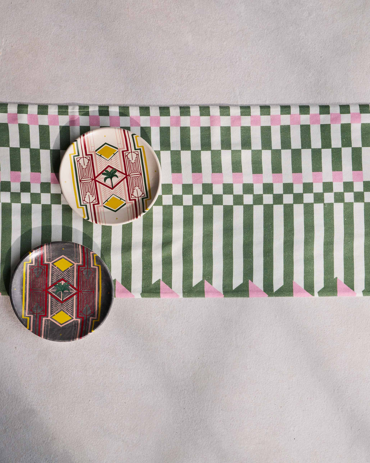 Plethora table runner laid flat in green, white and pink geometric stripes.