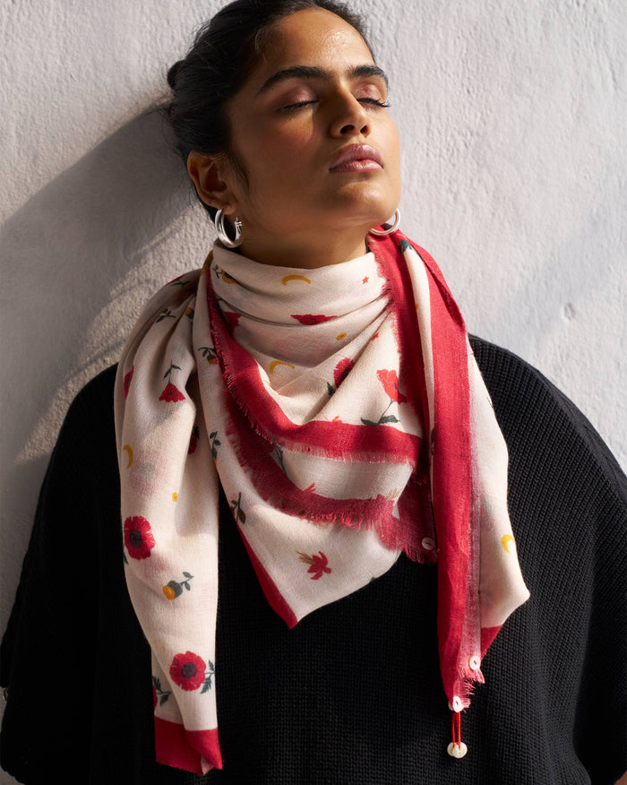 Person wearing an ivory Poppy Shawl with a red border and poppy print.