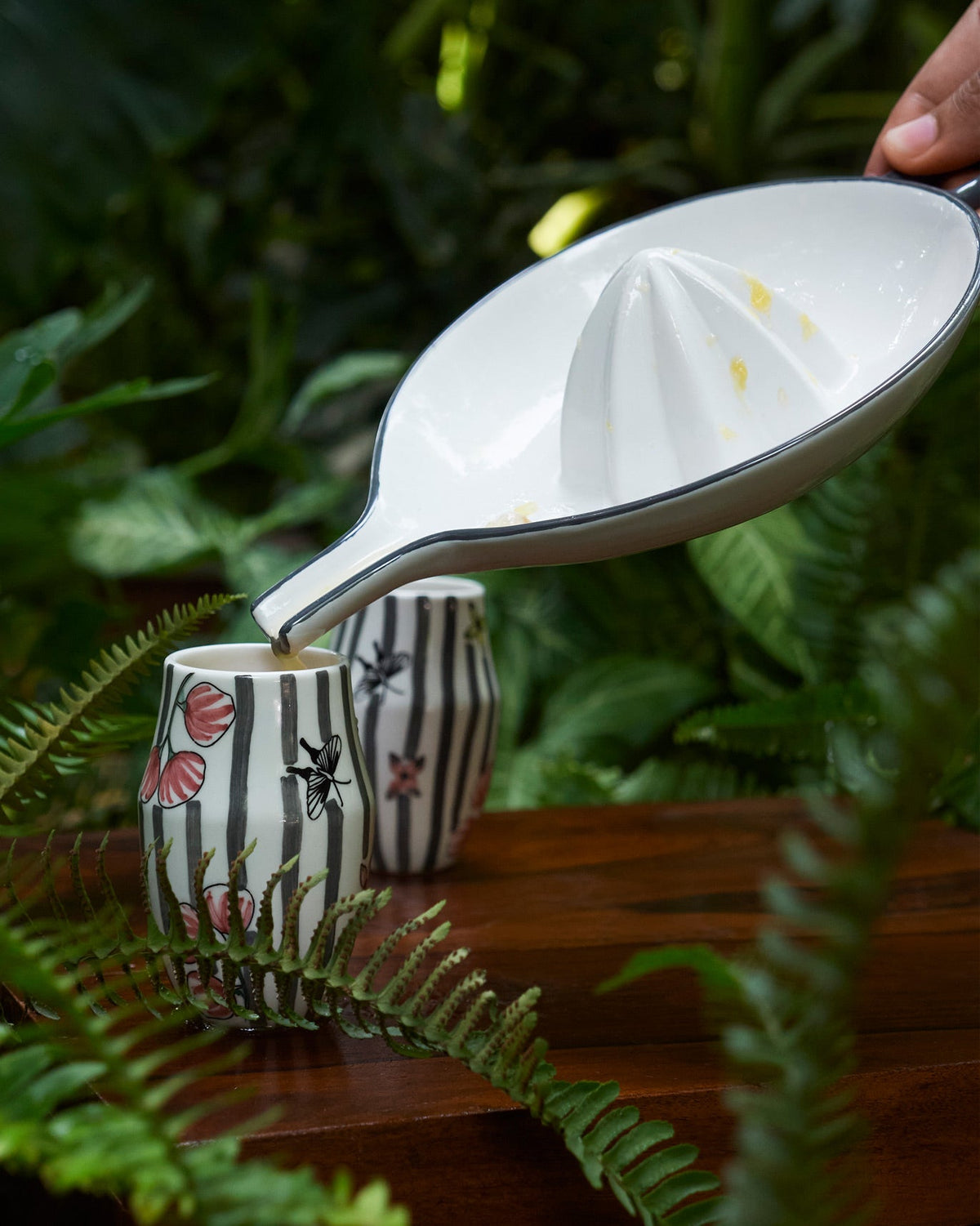Hand tilting the citrus squeezer dish over a striped cup.