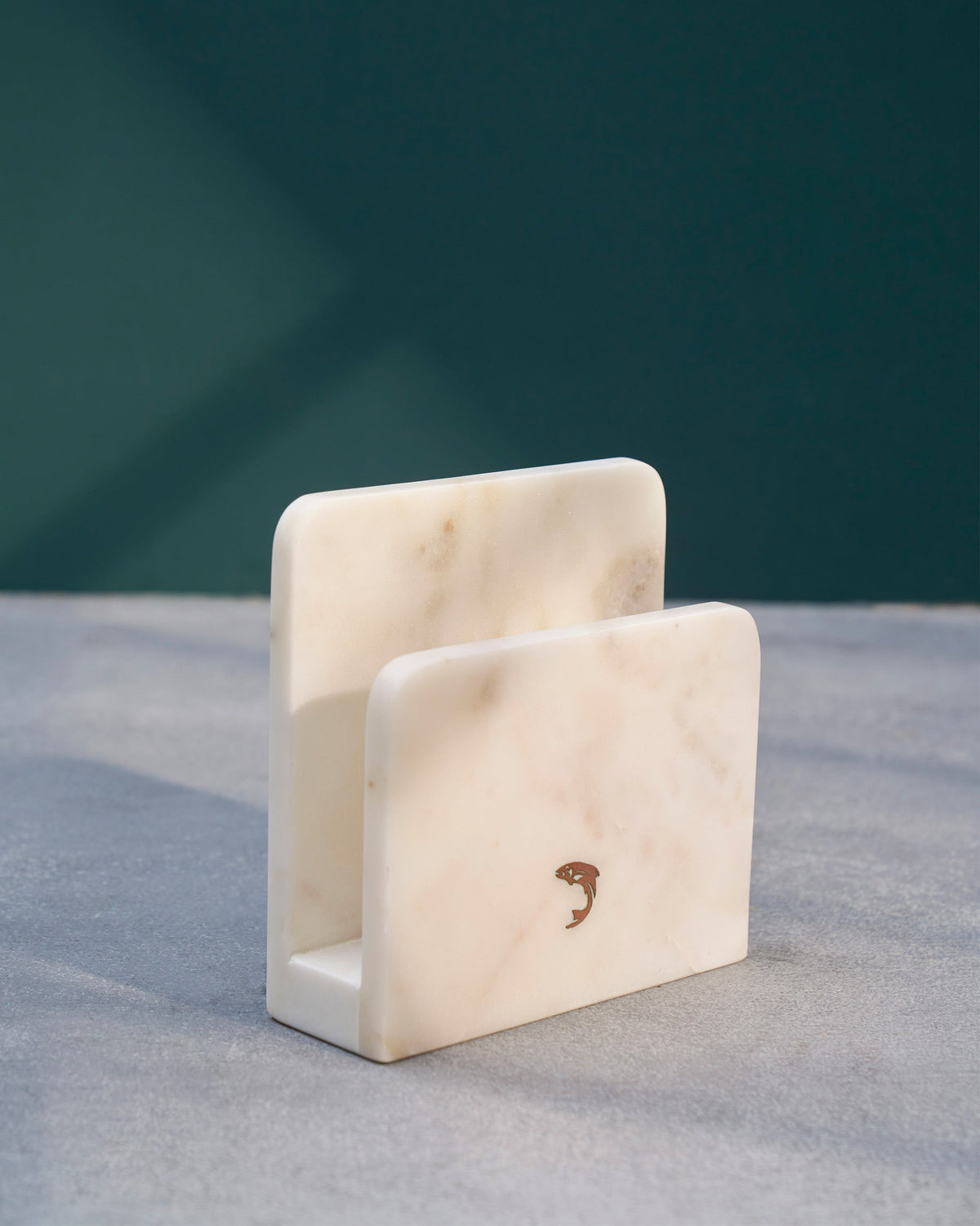 Angled view of the white marble Napkin Holder, with a small fish motif on its front panel.