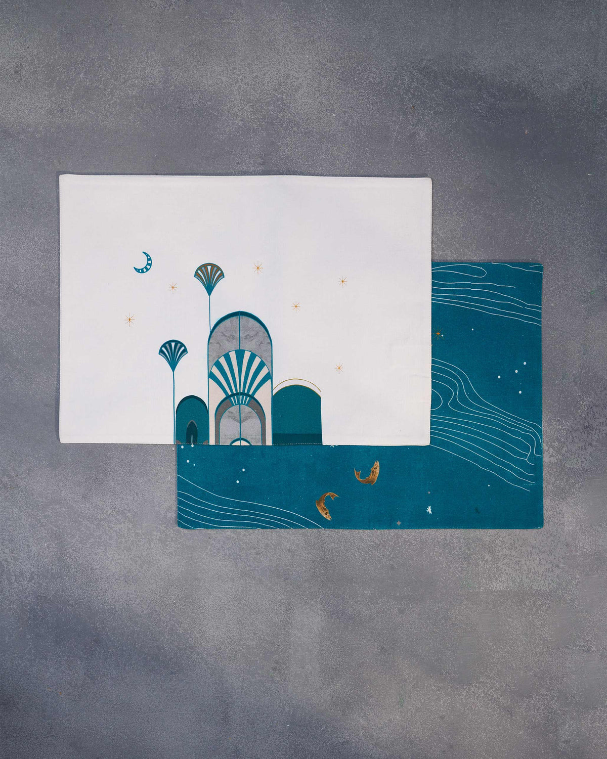 Two Tranquil Placemats laid overlapping, a cream arch design over a teal wave design.