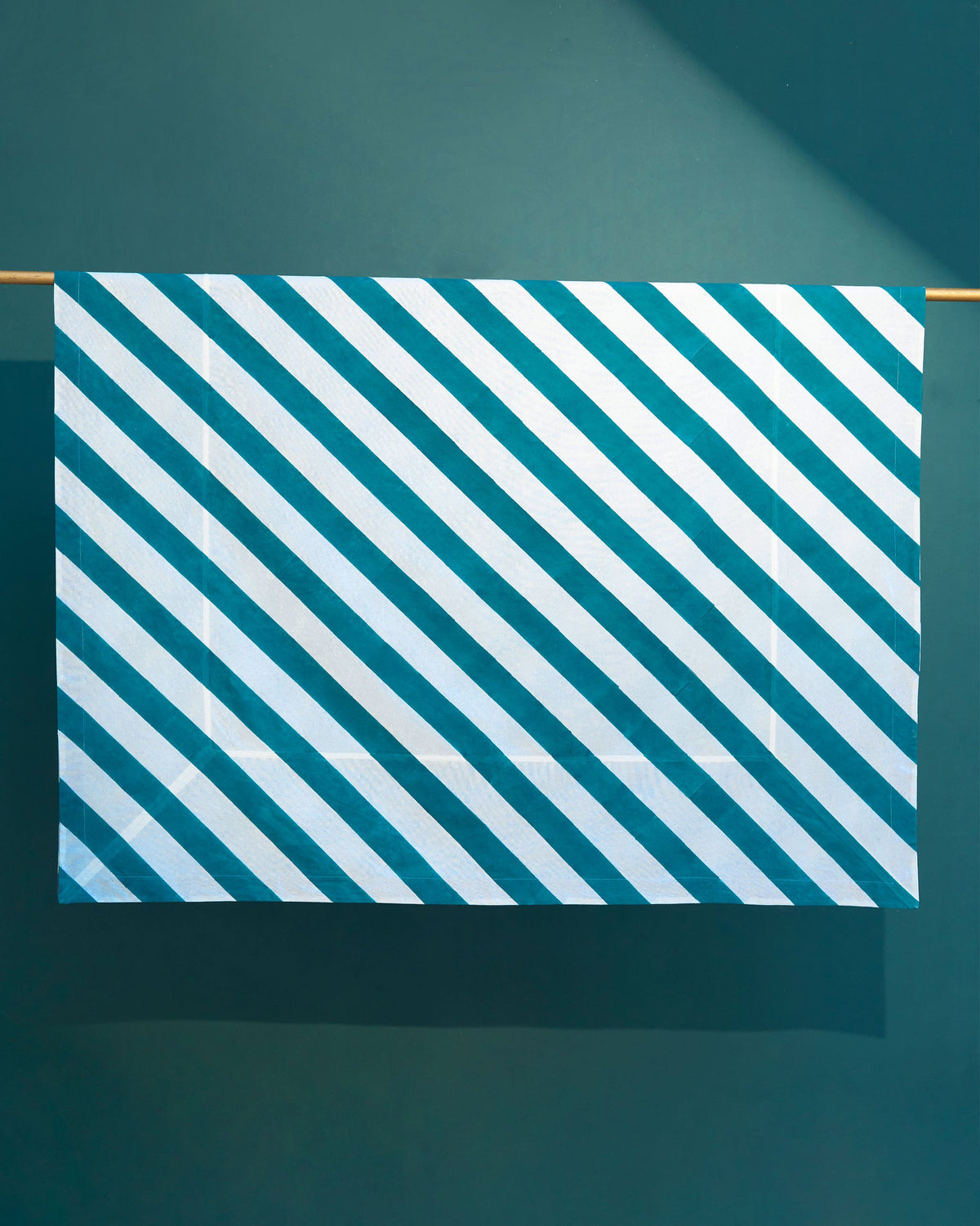 Plush Tablecloth in teal and white diagonal stripes, hung from a rod.