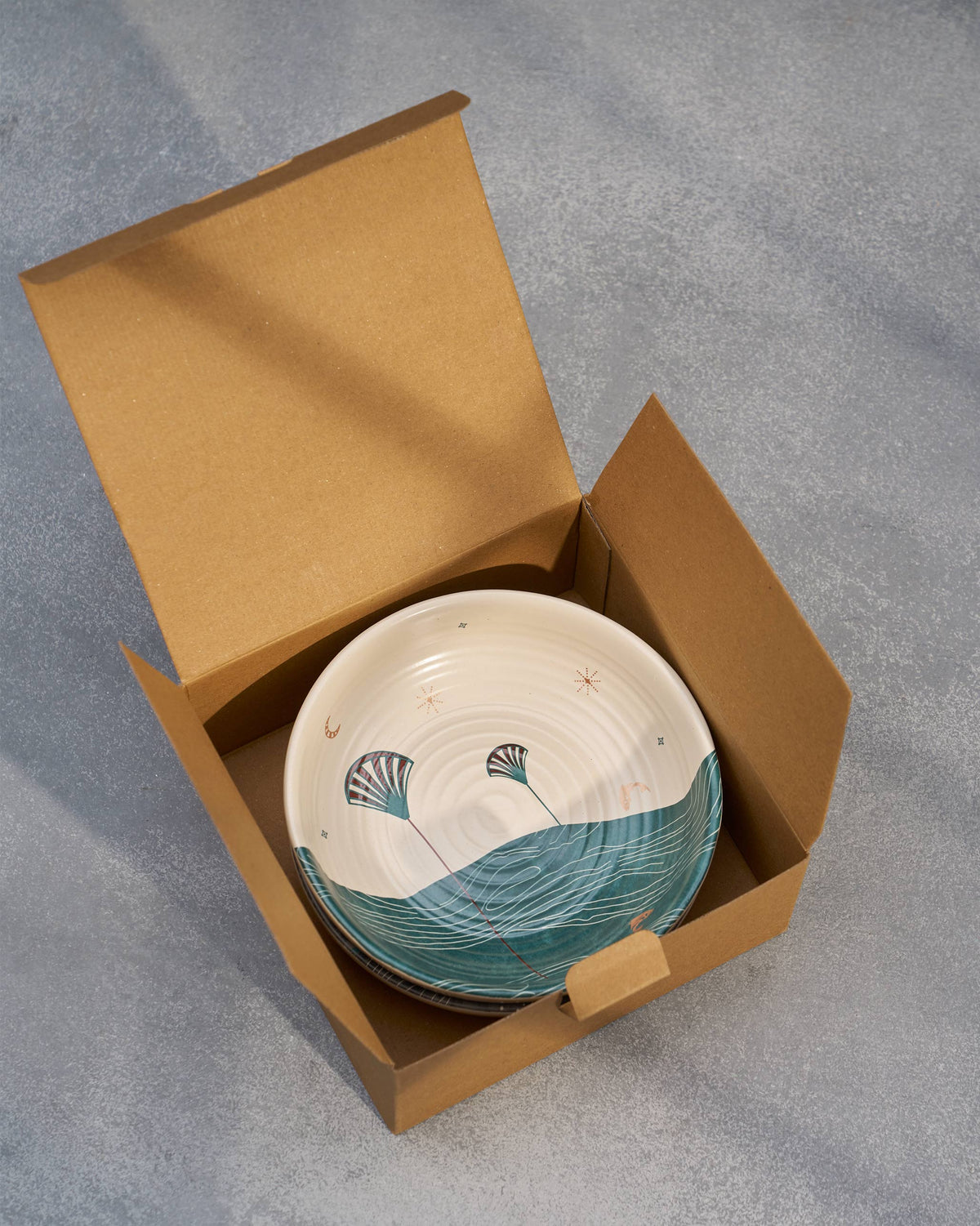 Pacific shallow bowls inside an open kraft box, the cream and teal one on top.