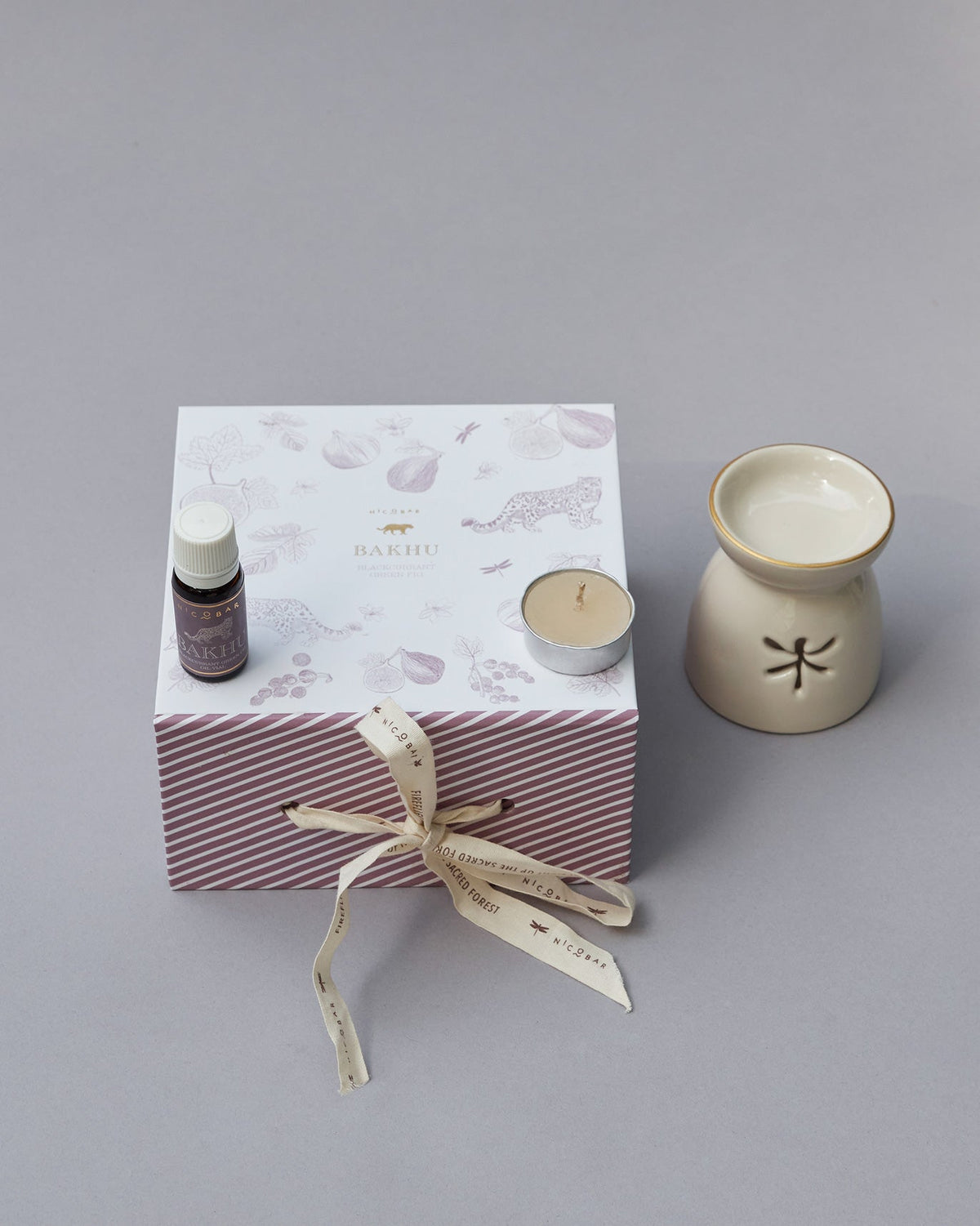 Sattva gift box tied with a ribbon, with a bottle and tealight on its lid.