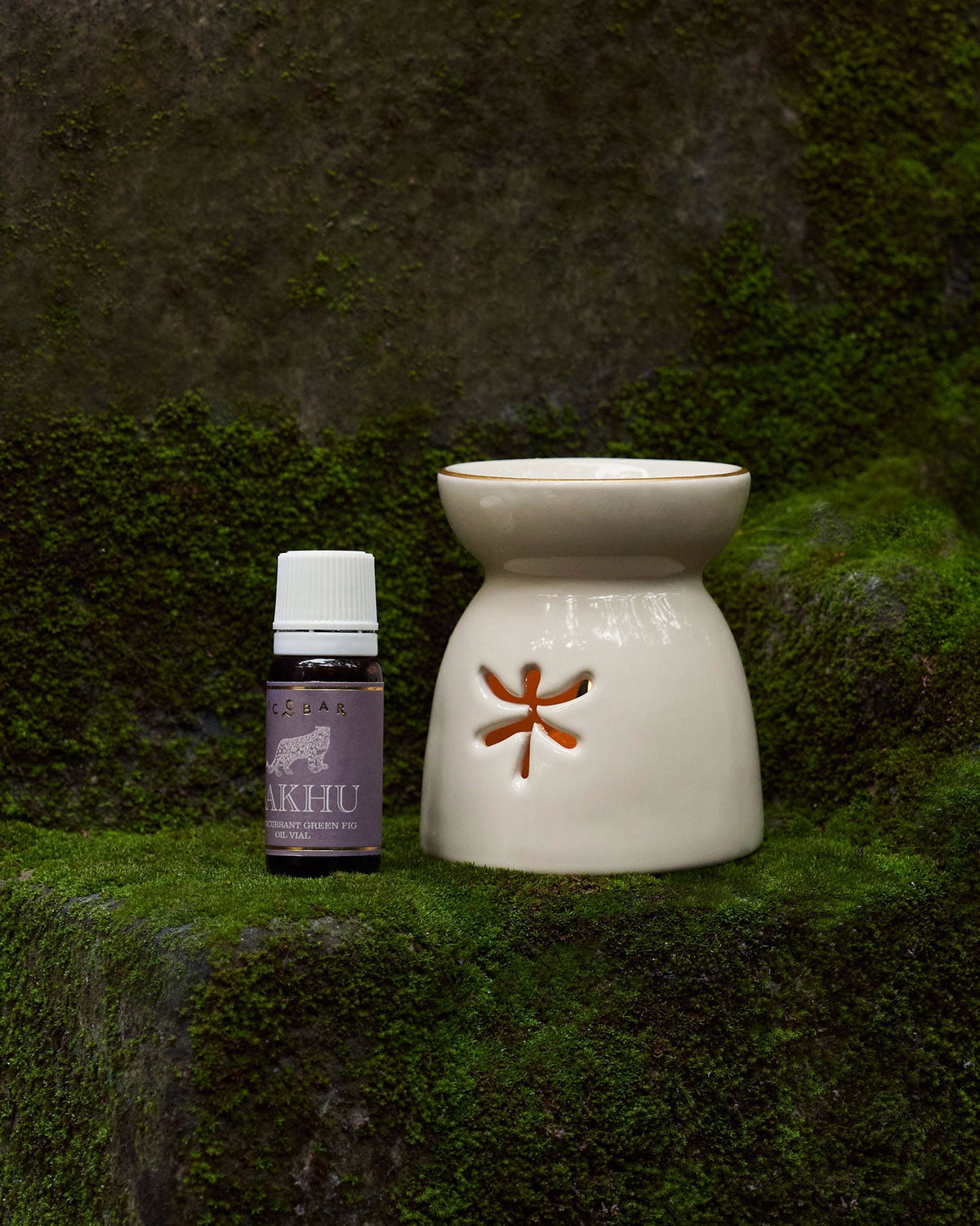 Cream ceramic oil burner beside a small bottle of oil on moss.