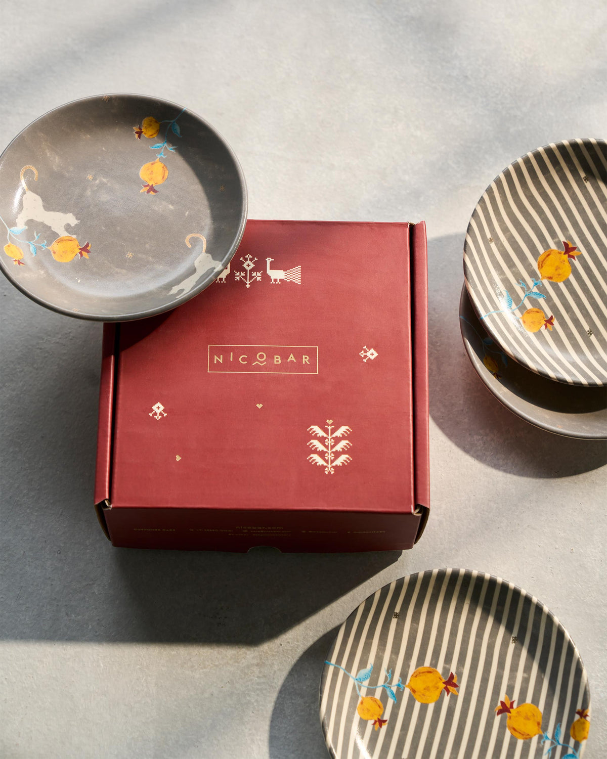 Anar tea plates with yellow pomegranate motifs beside a Nicobar gift box.