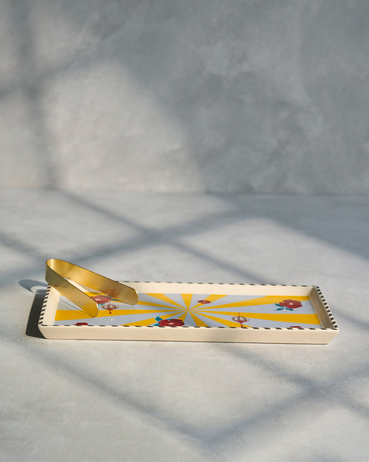 Side view of Chakra Cookie Tray with a gold tong resting on its edge.