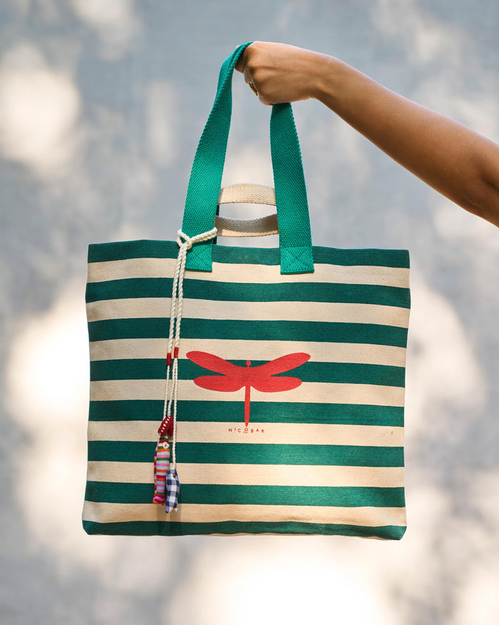 Bagan Stripe Tote with teal handles held up by hand, showing a red dragonfly print.