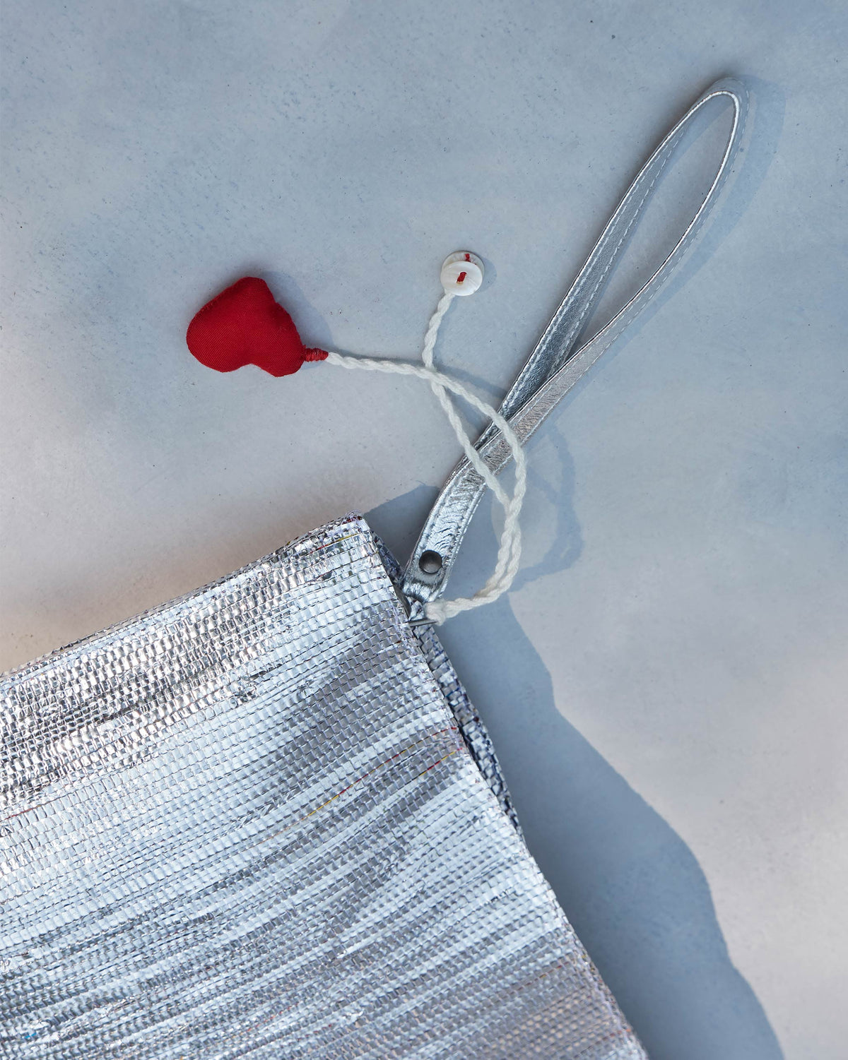 Close-up of the silver Sitara Clutch corner with its red heart tassel.