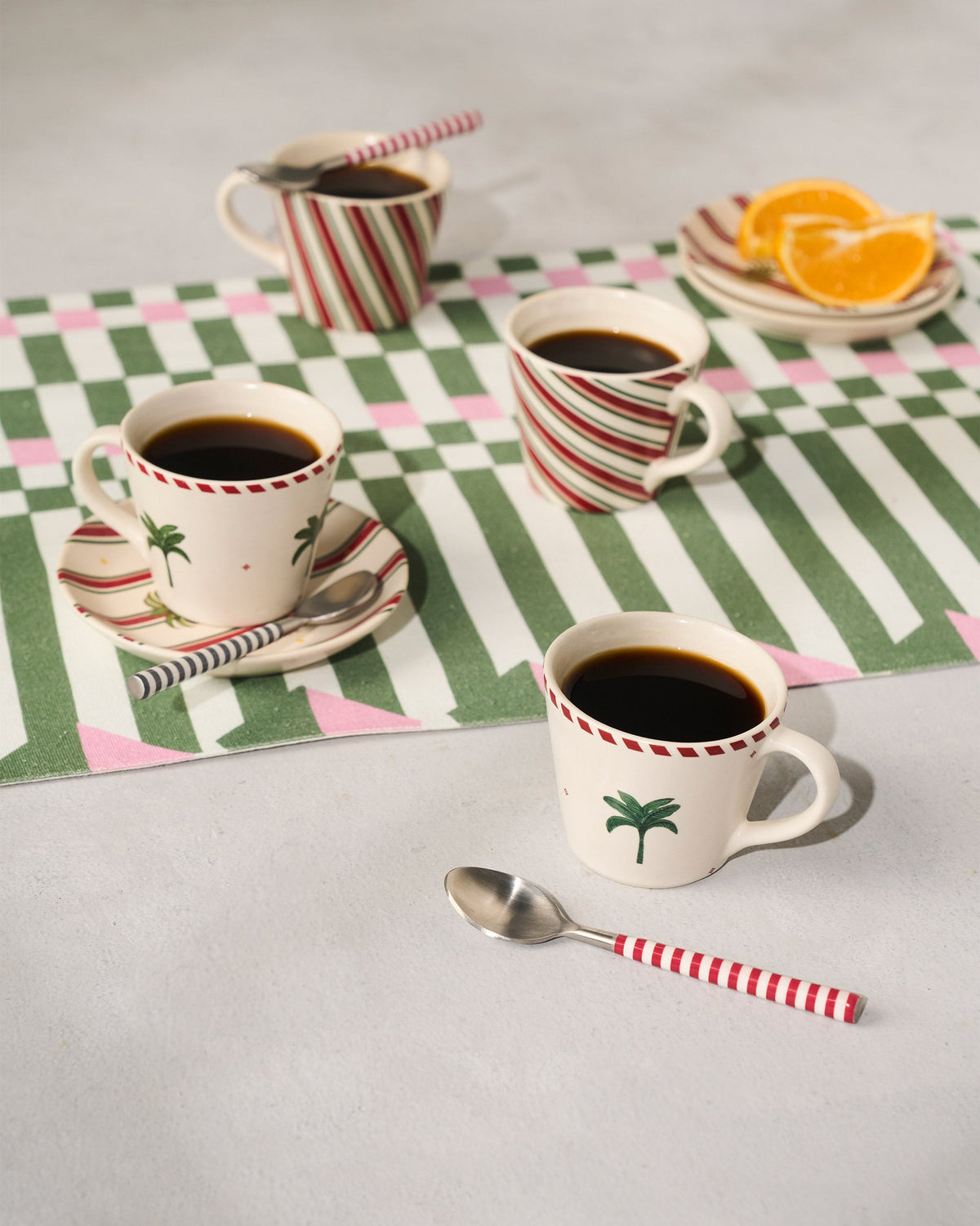 Whimsical Espresso Mugs with palm motifs and red stripes on a checked tablecloth.