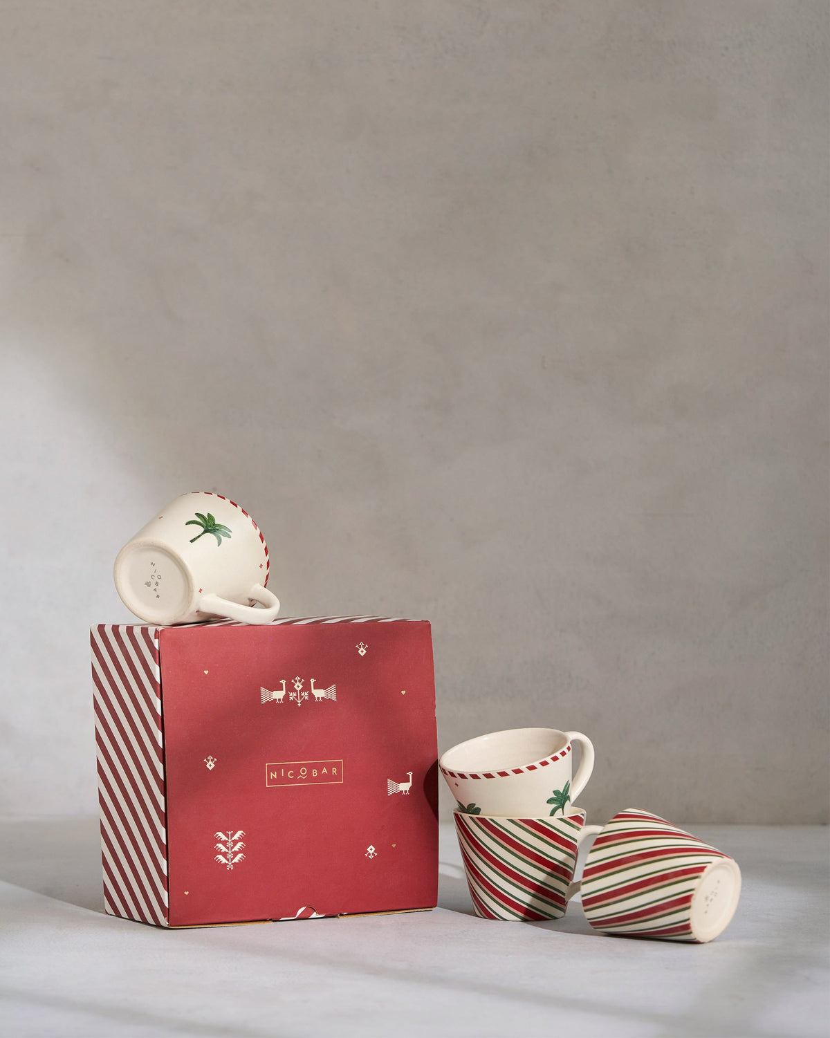 Whimsical Espresso Mugs with palm motifs beside a red striped gift box.