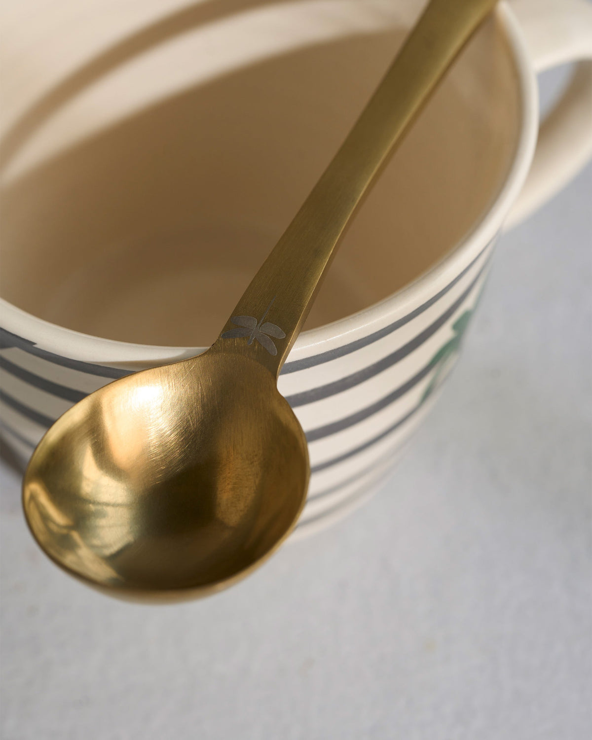 Close-up of the gold spoon resting on the Leafty Affair mug, showing an engraved handle.
