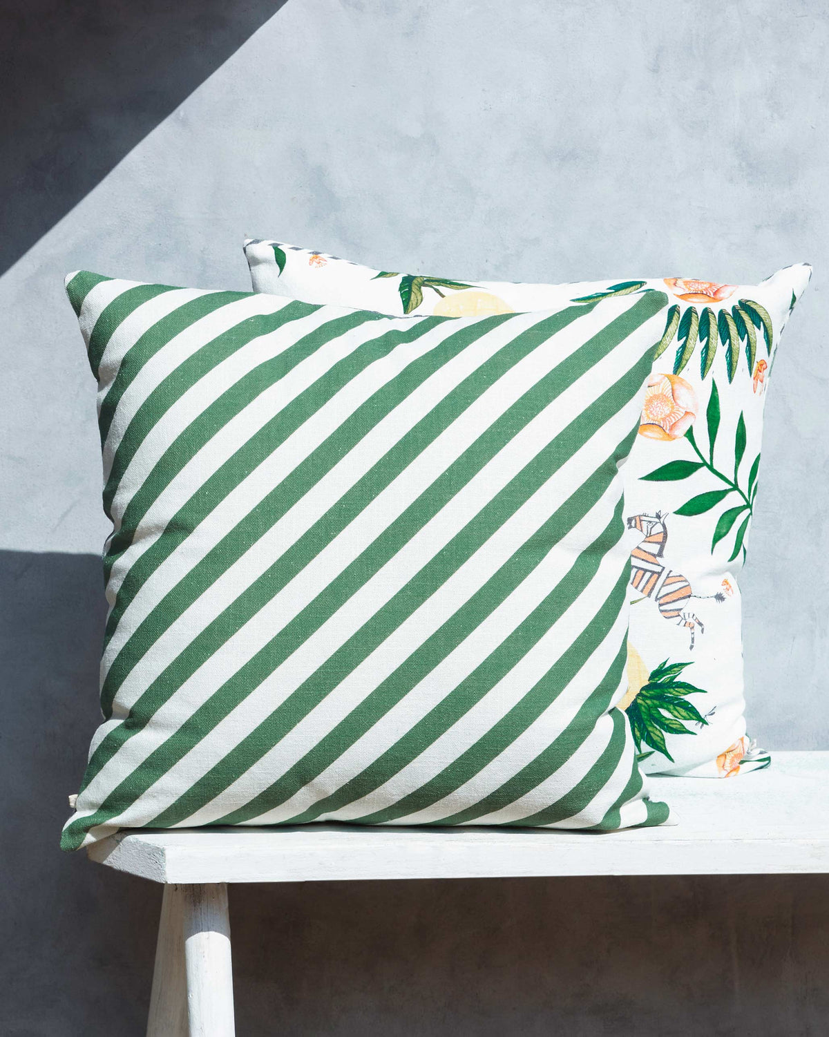 Ananas Cushion Cover behind a green striped cushion on a white bench.