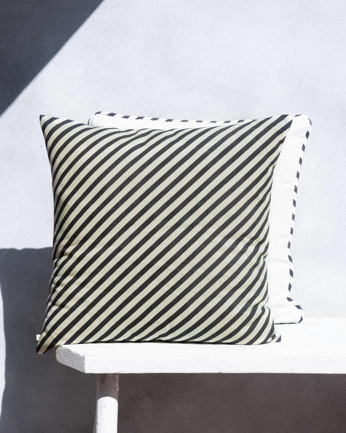 Cushion with black and cream diagonal stripes on a white bench.