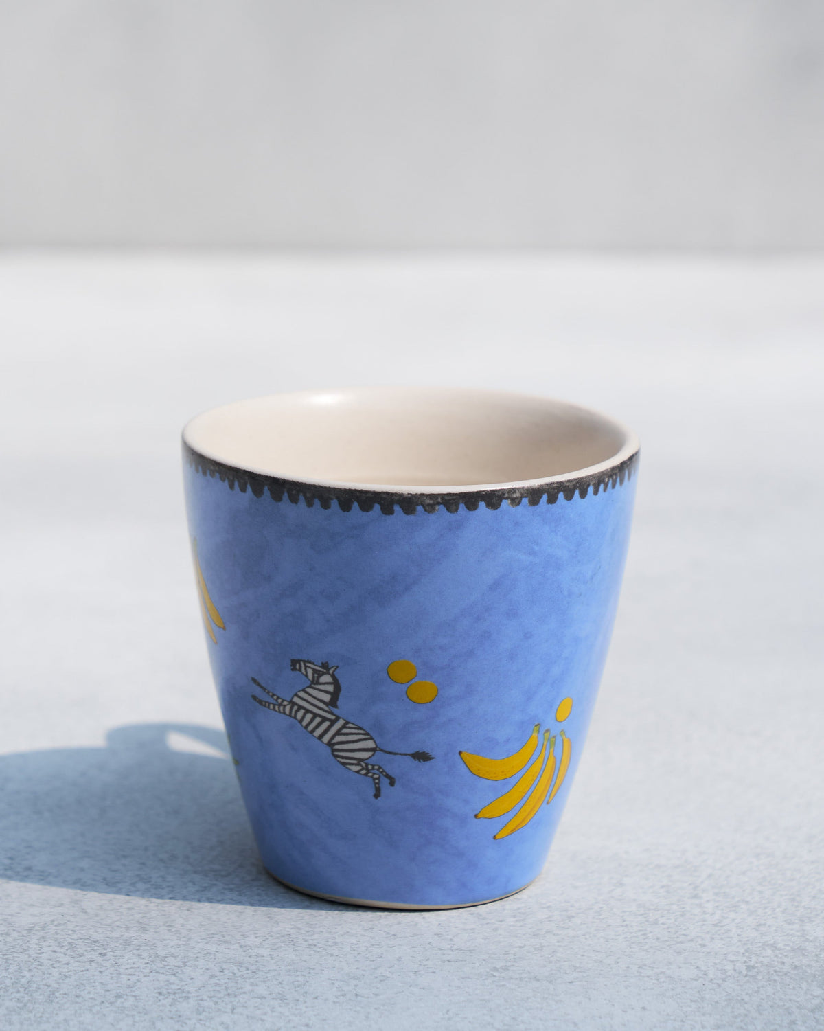 Blue Zebra Conical Mug without a handle, showing a leaping zebra and bananas.