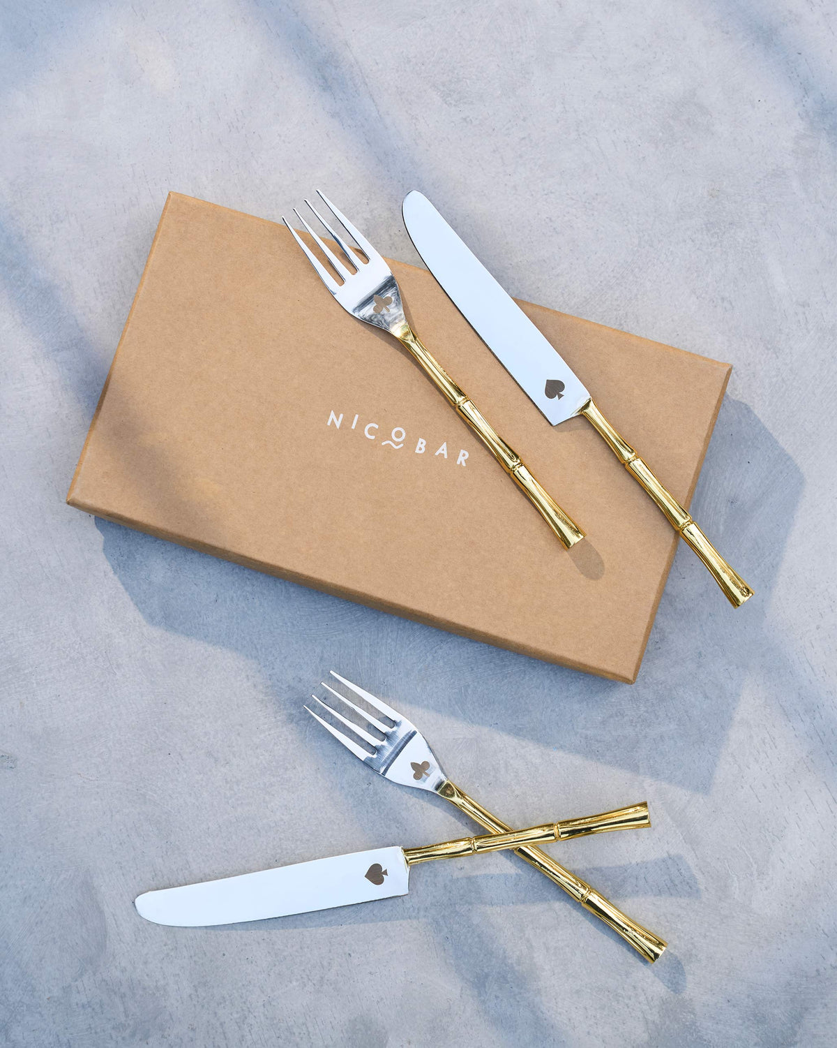 Spade & Club cutlery laid on a Nicobar box, with a fork and knife crossed below.