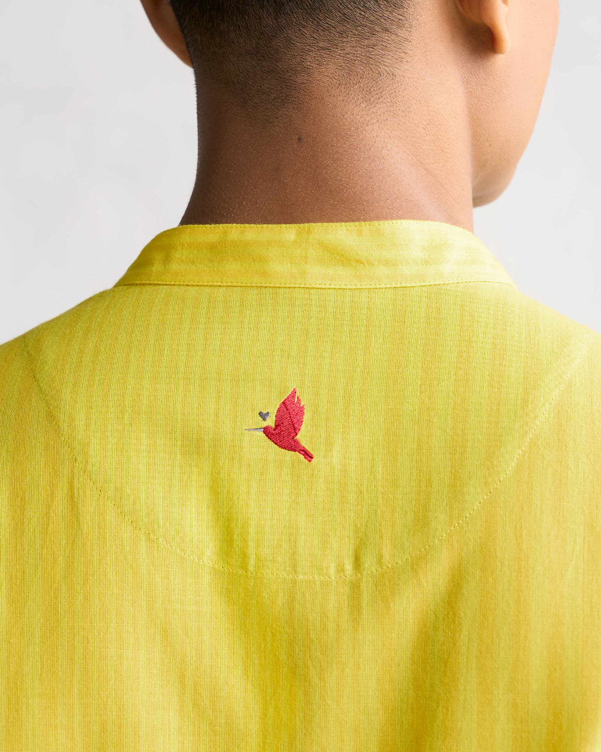 Close-up of a yellow Side Placket shirt collar showing a small red bird embroidery.