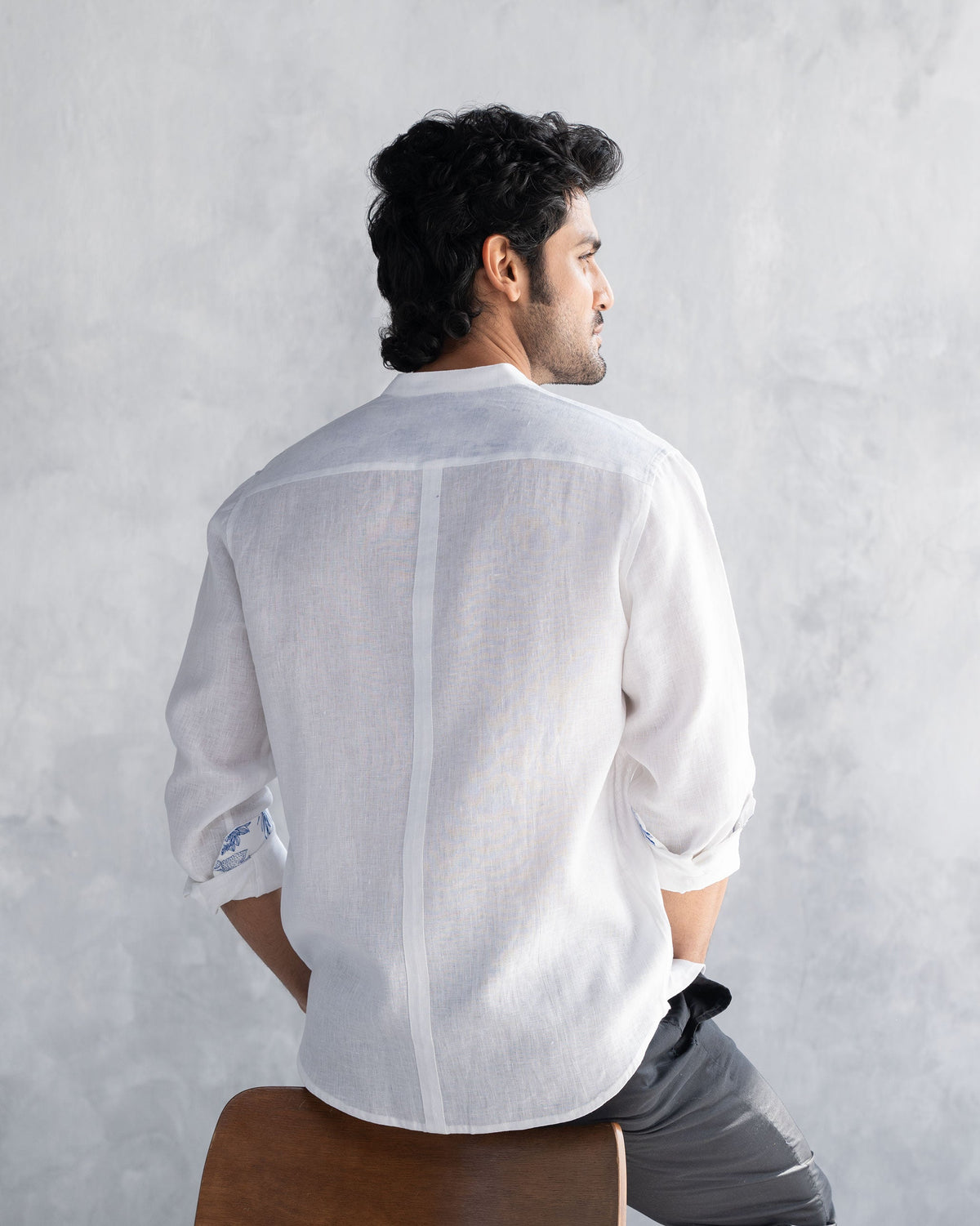 Back of a white Nawab shirt with rolled sleeves showing blue cuff trim.