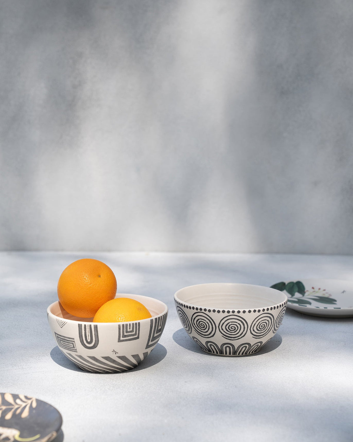 Serenity cereal bowl holding two oranges, beside a spiral-patterned bowl.
