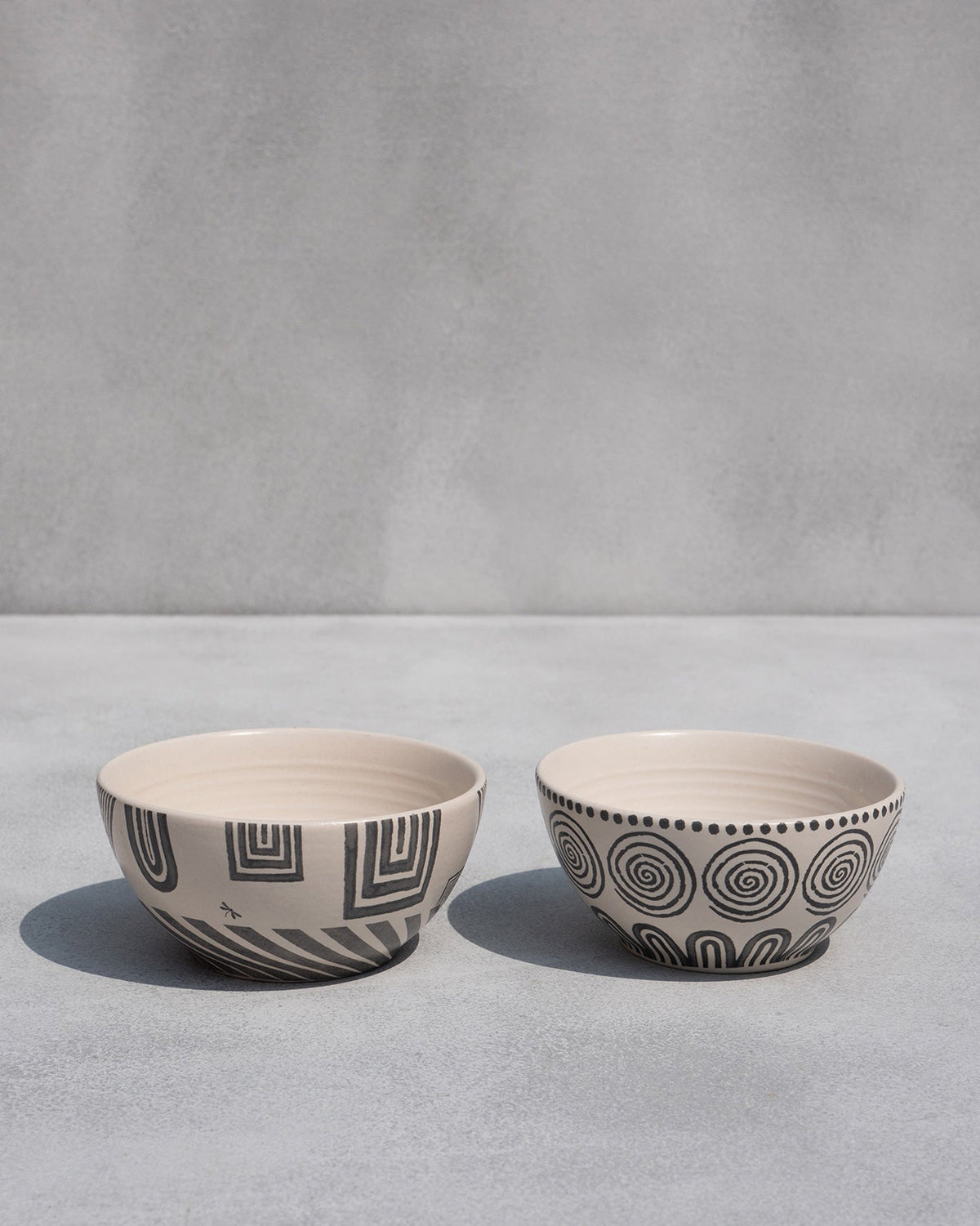 Serenity cereal bowl with geometric lines beside one with spirals and a dotted rim.