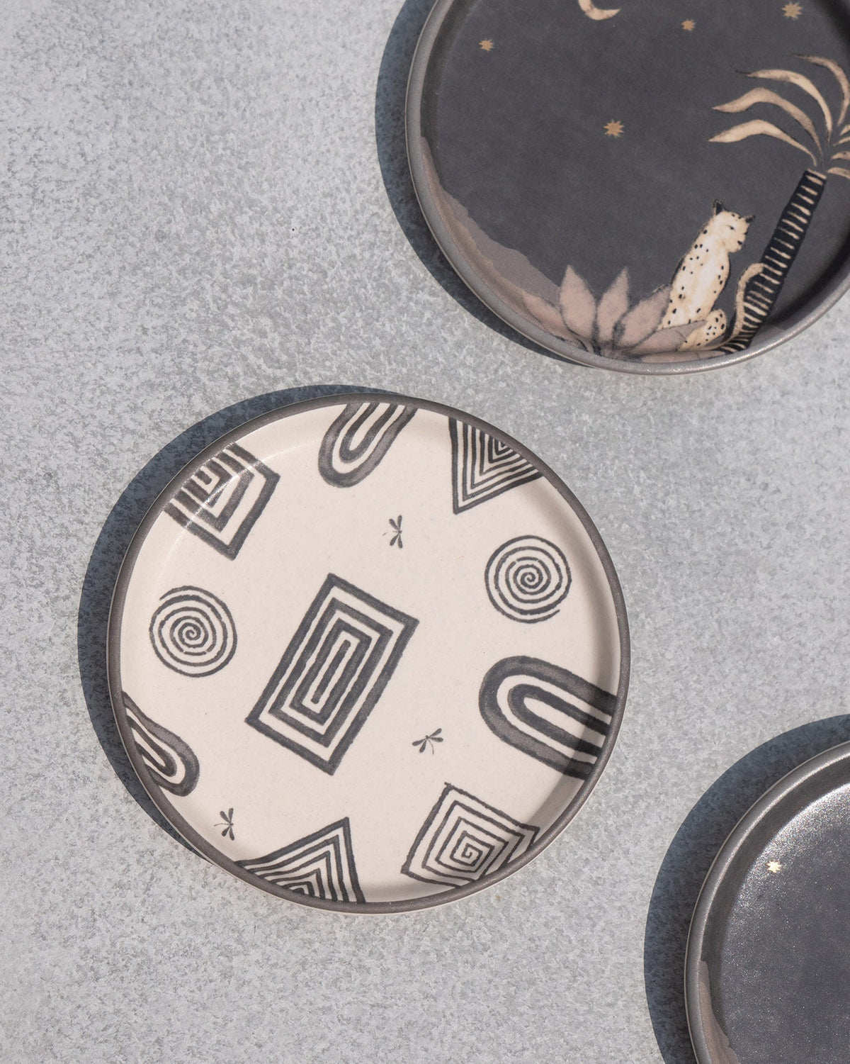 Close-up of a cream Serenity Coaster showing black spiral and arch motifs.