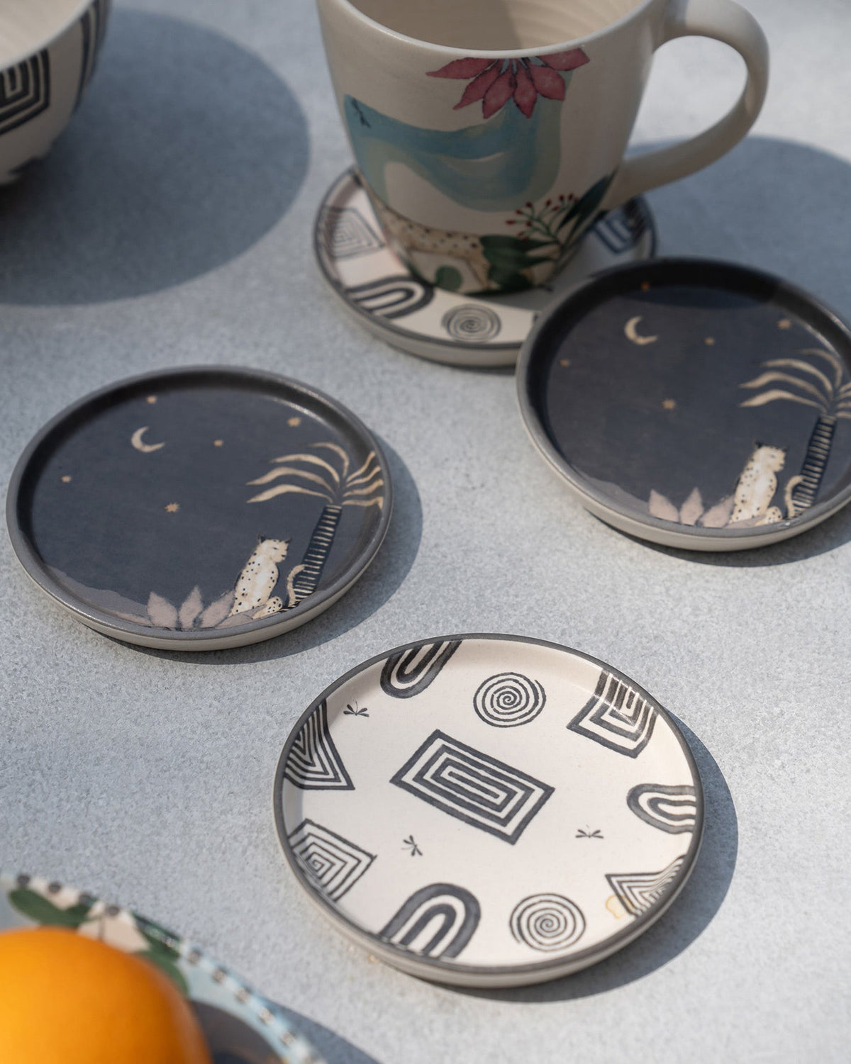 Serenity Coasters with a dark design and a cream design, placed in front of a mug.
