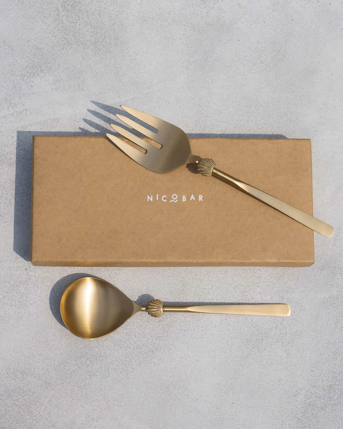 Seashell Salad Server fork and spoon laid on a Nicobar box.