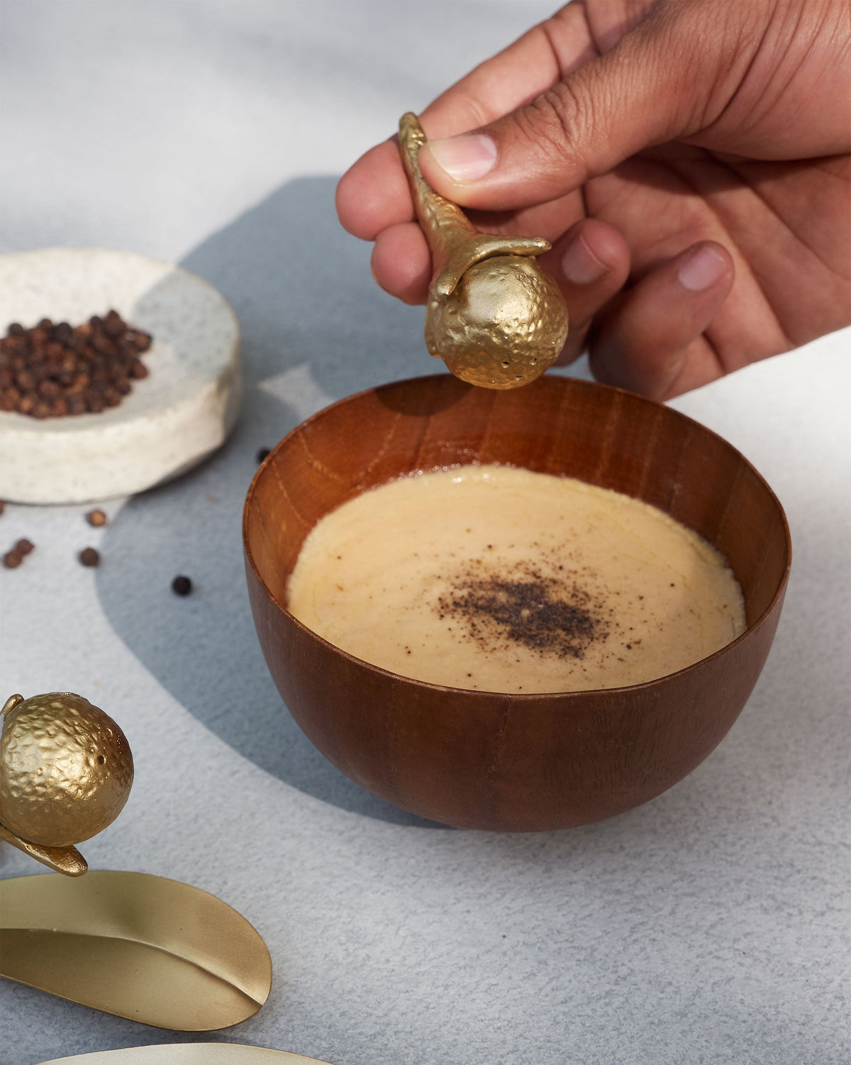 Hand holding a gold Clove shaker over a wooden bowl of dip.