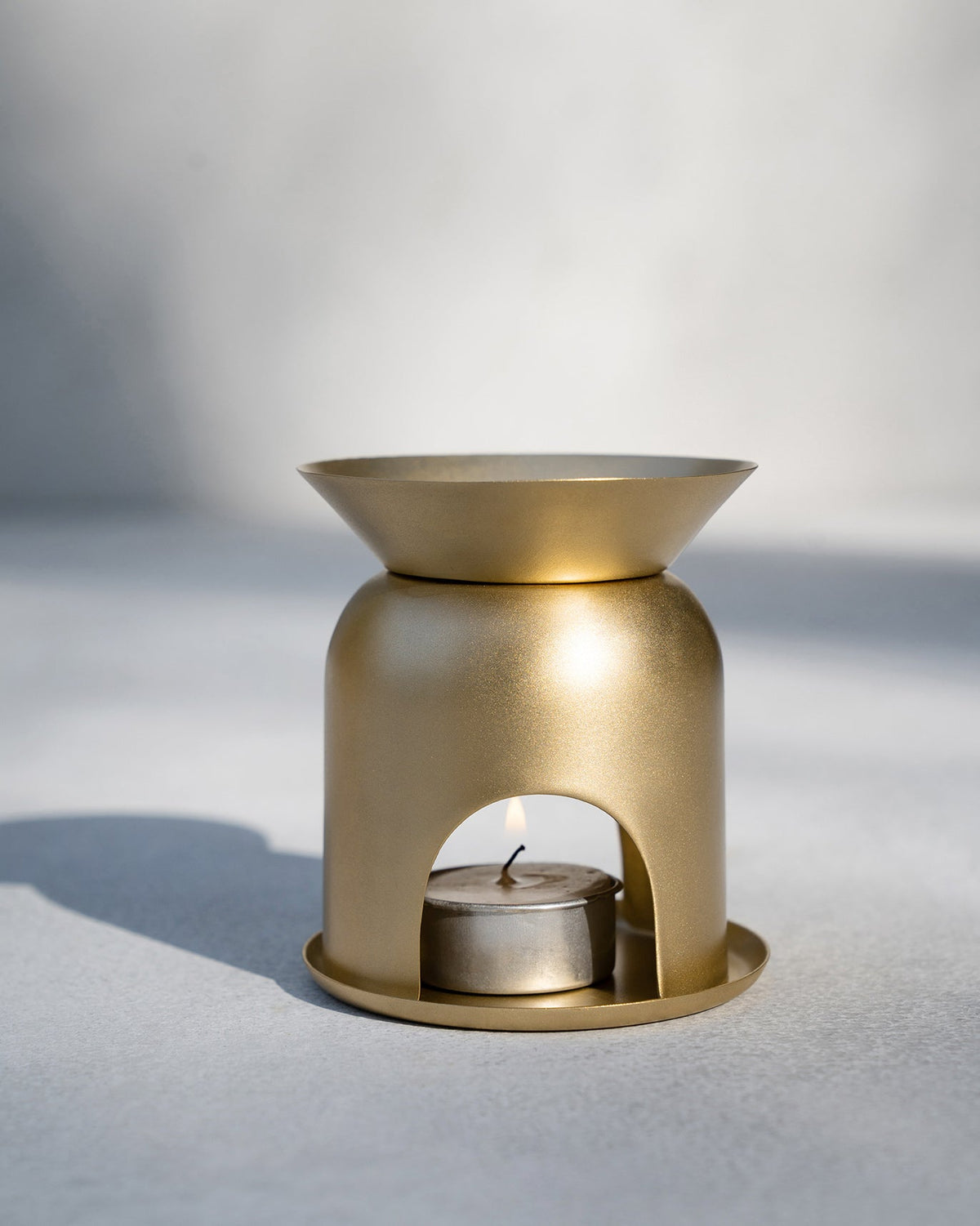Gold Clove Diffuser with a lit tealight in its base.