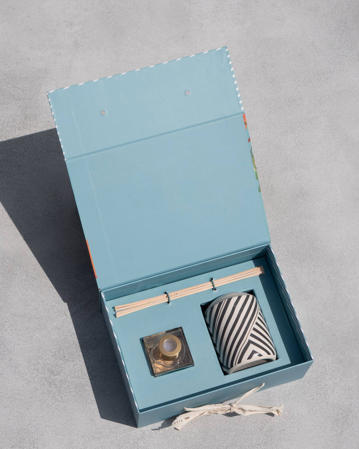 Open Meraki Gift Set box showing reed sticks, a small glass bottle and a striped ceramic pot.