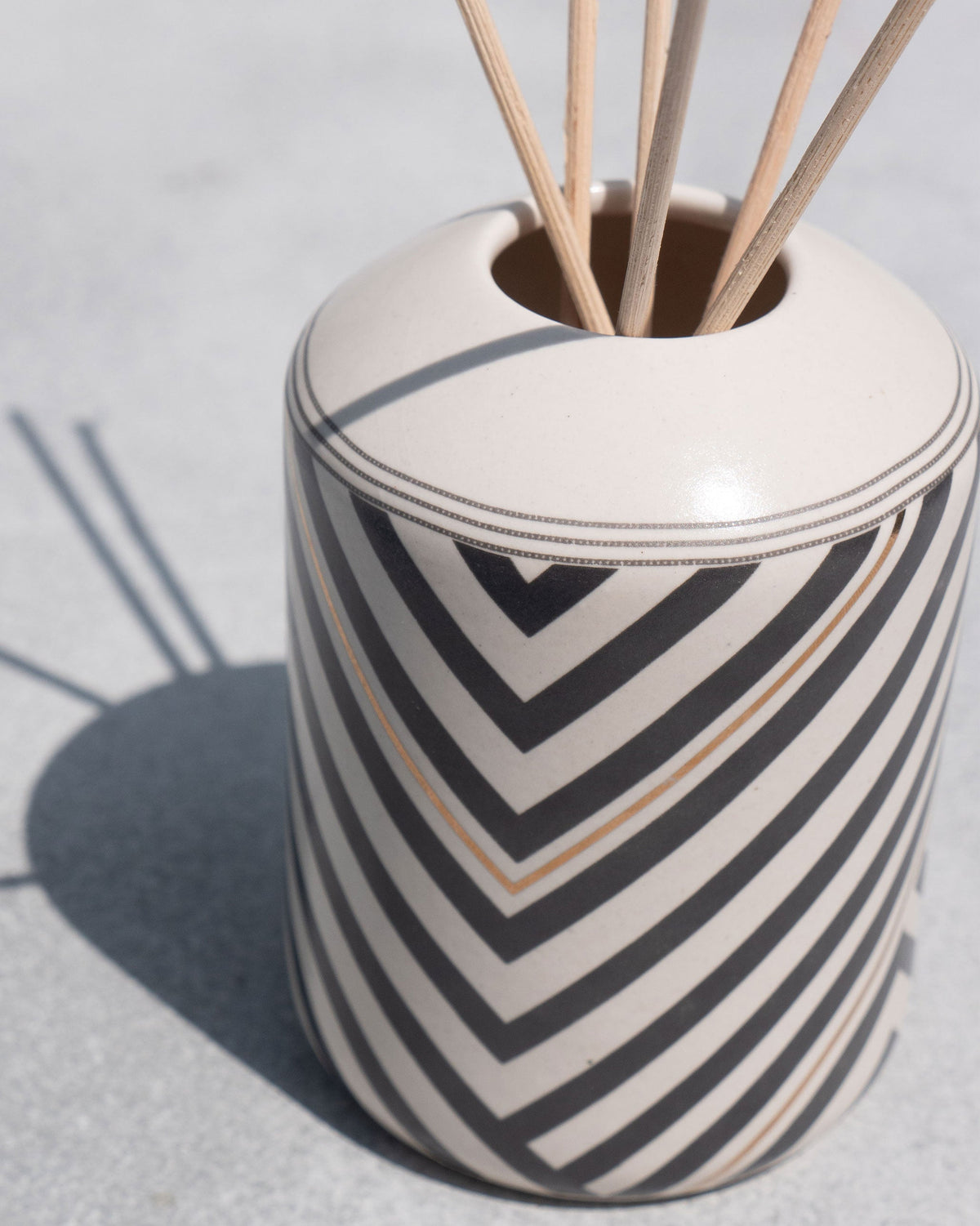 Close-up of the Meraki Gift Set's chevron-striped ceramic pot with reed sticks.