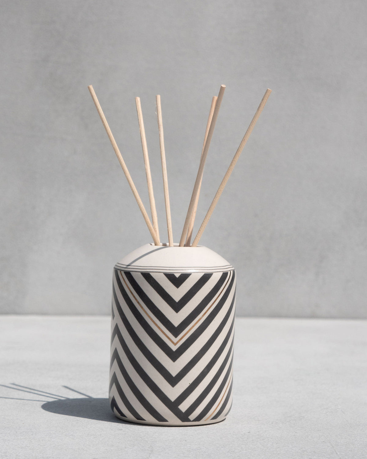 Meraki Gift Set's chevron-striped ceramic pot with reed sticks standing upright.