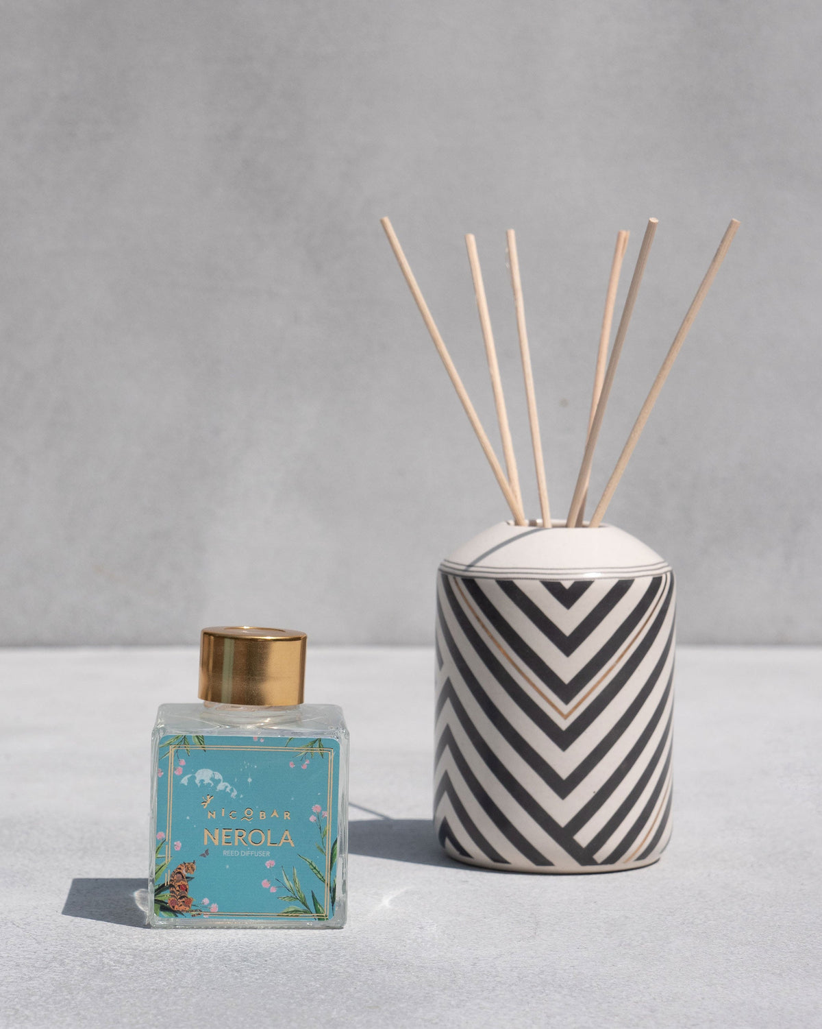Meraki Gift Set's Nerola reed diffuser beside a chevron-striped ceramic pot.