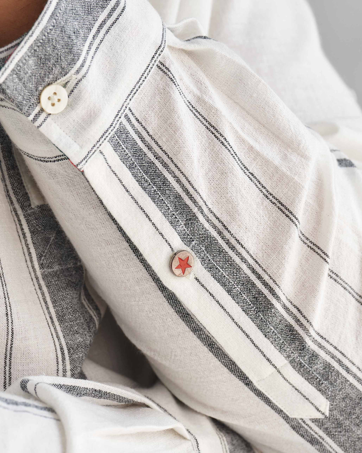 Close-up of an ivory Novac shirt sleeve with grey stripes and a red star button.