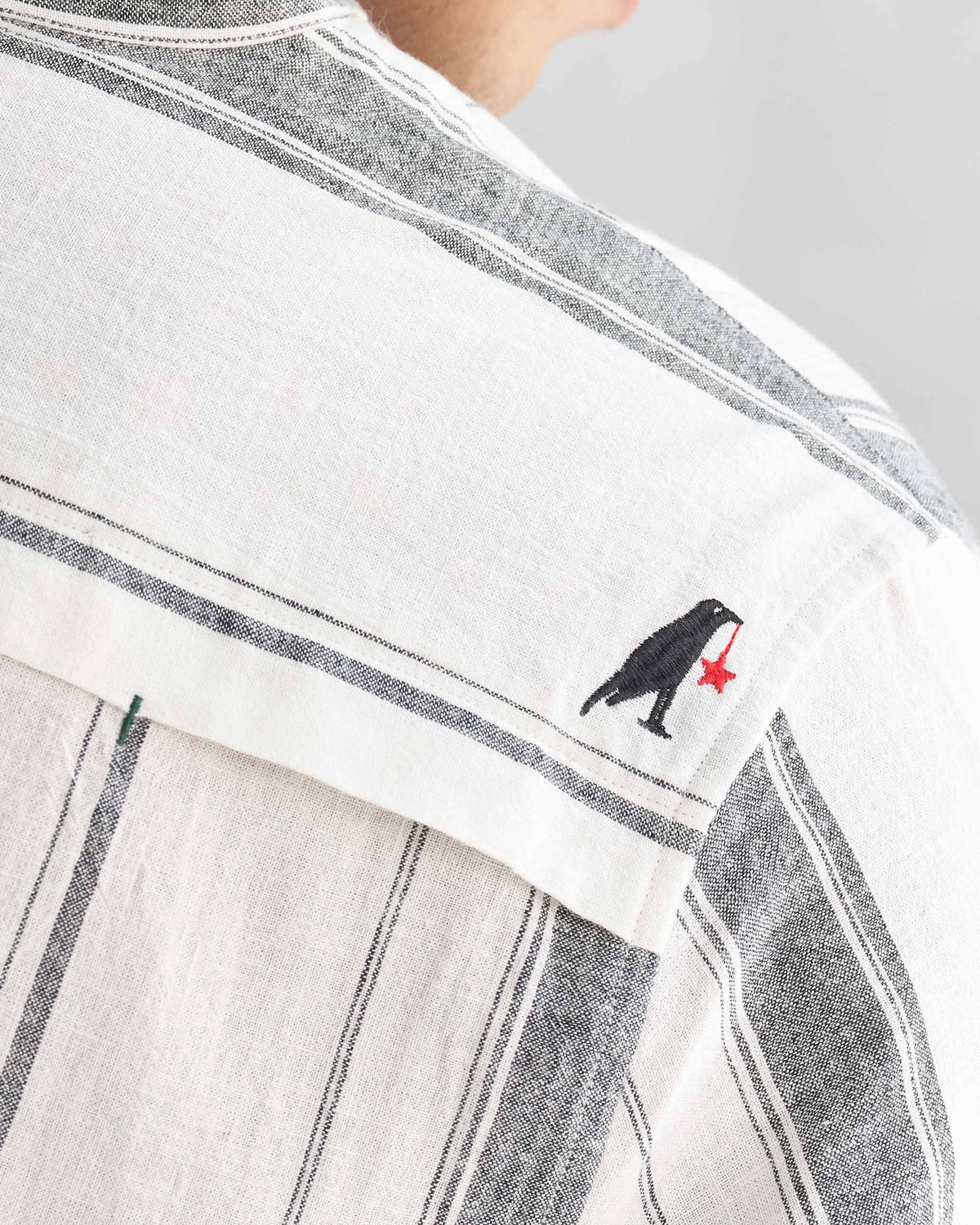 Close-up of an ivory Novac shirt showing a small black bird embroidery with a red star.