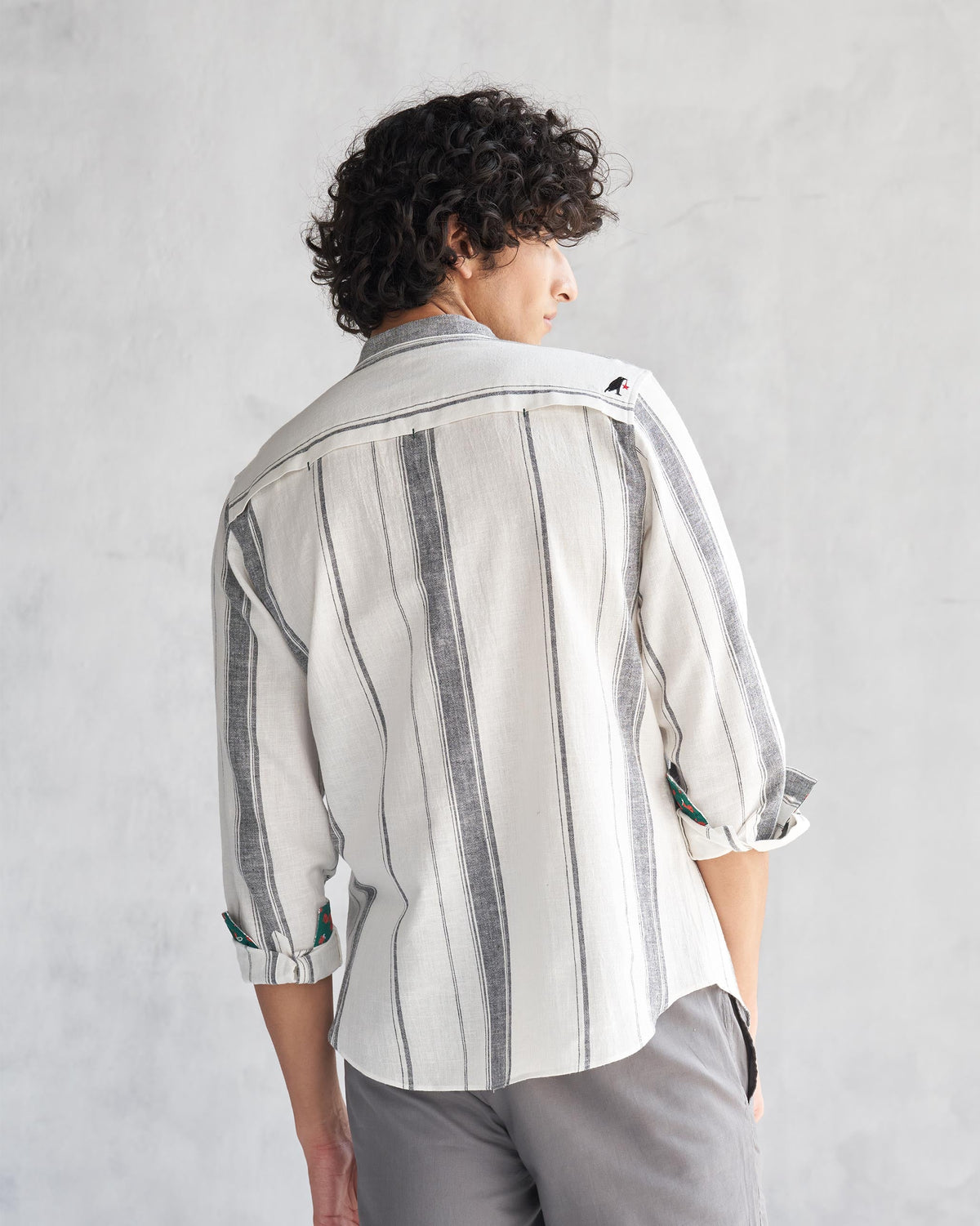 Back of an ivory Novac shirt with grey stripes and a small bird embroidery worn by a person.