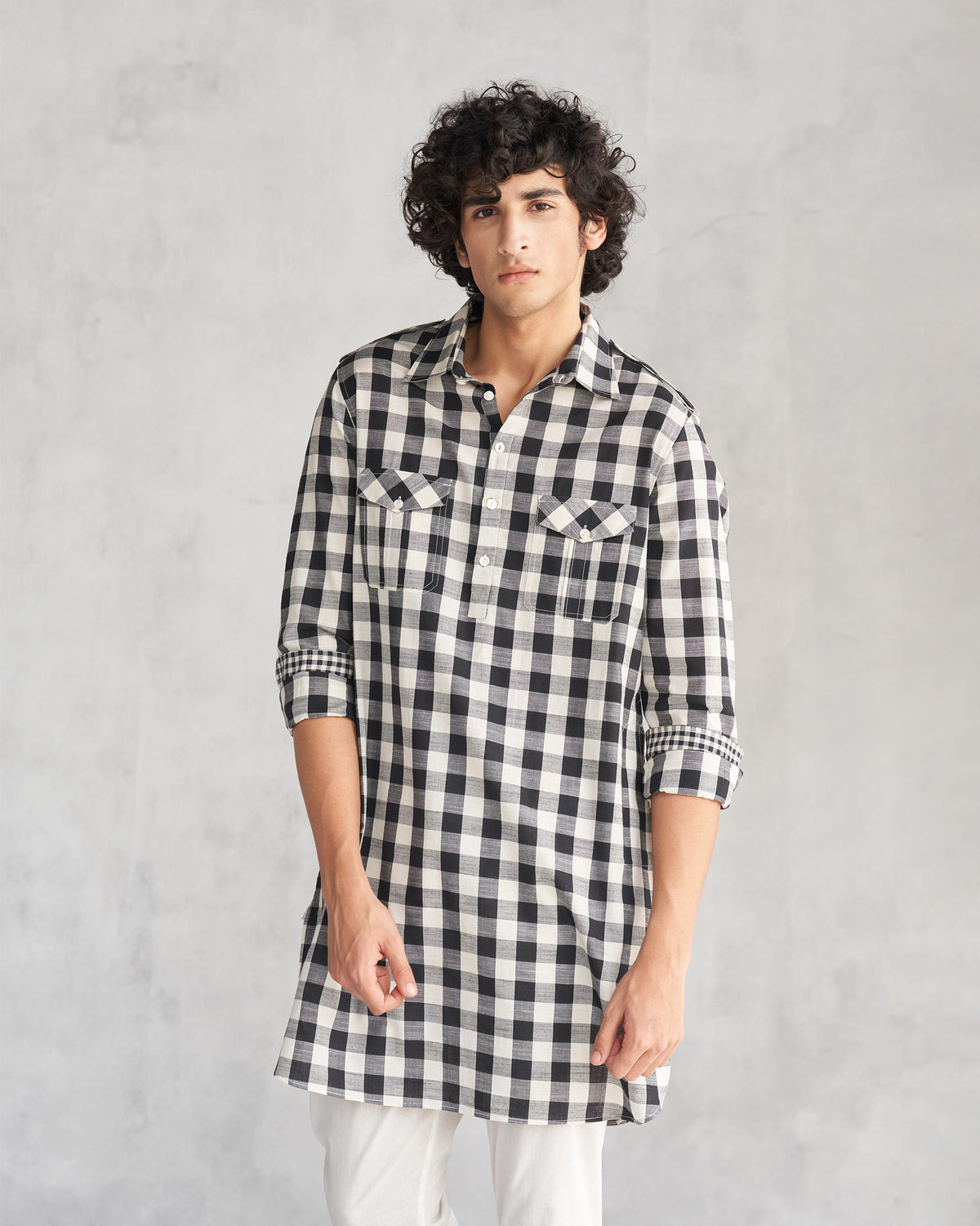 Person wearing a black and ivory checked Nizamuddin kurta with chest pockets.
