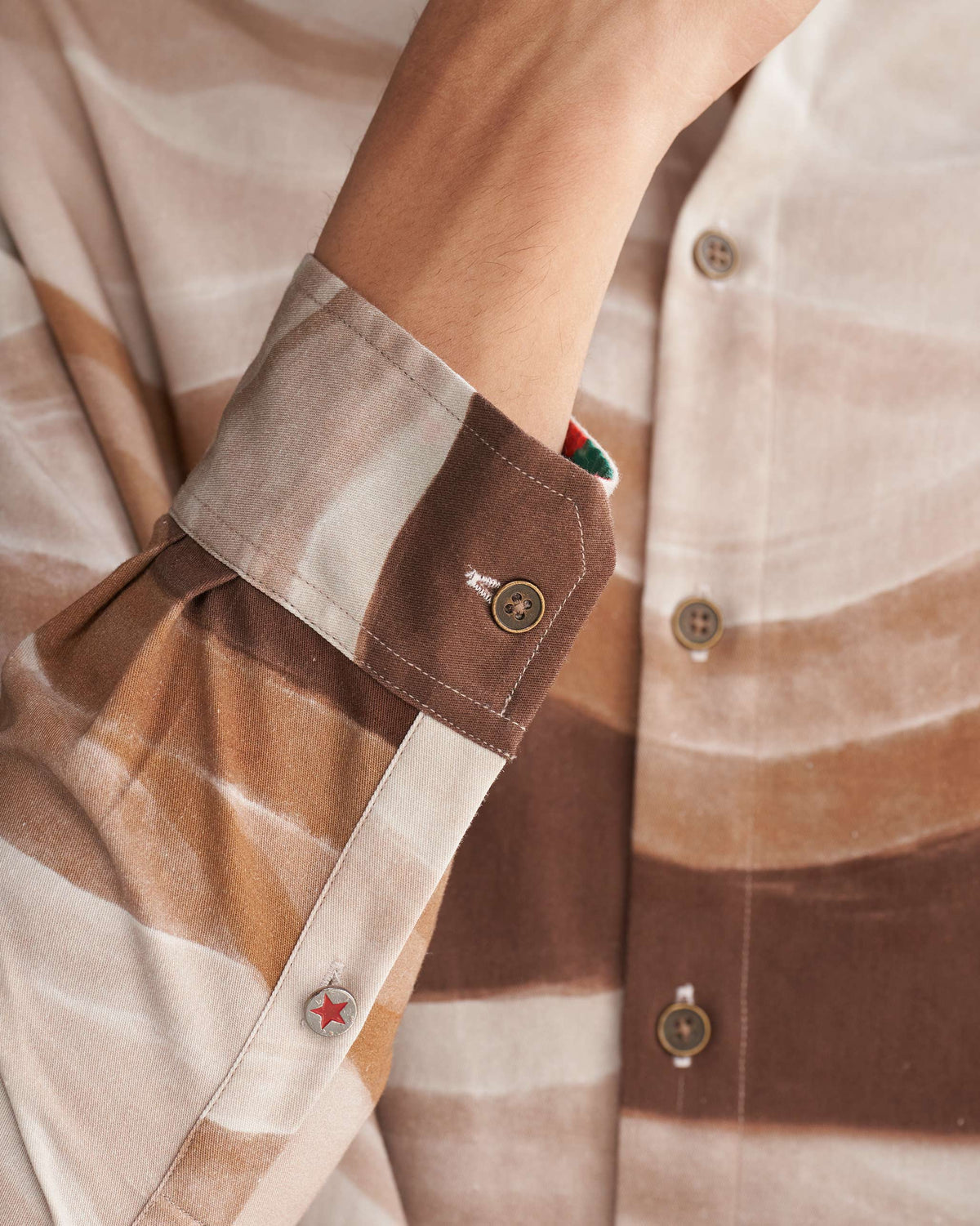 Close-up of a brown wave print Nawab shirt showing a cuff with a red star button.