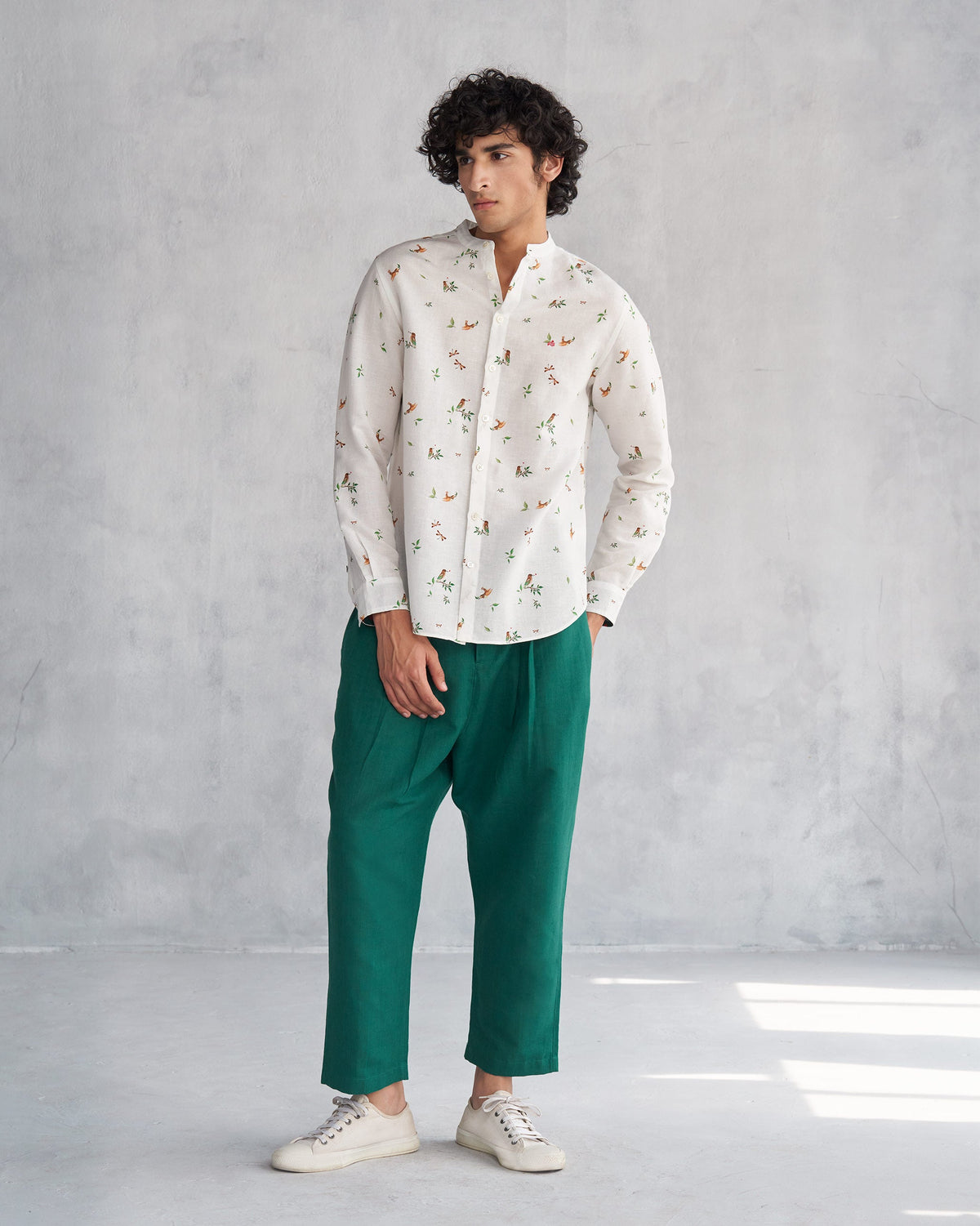 Person standing in a white Nawab Shirt with a bird and leaf print, one hand in pocket.