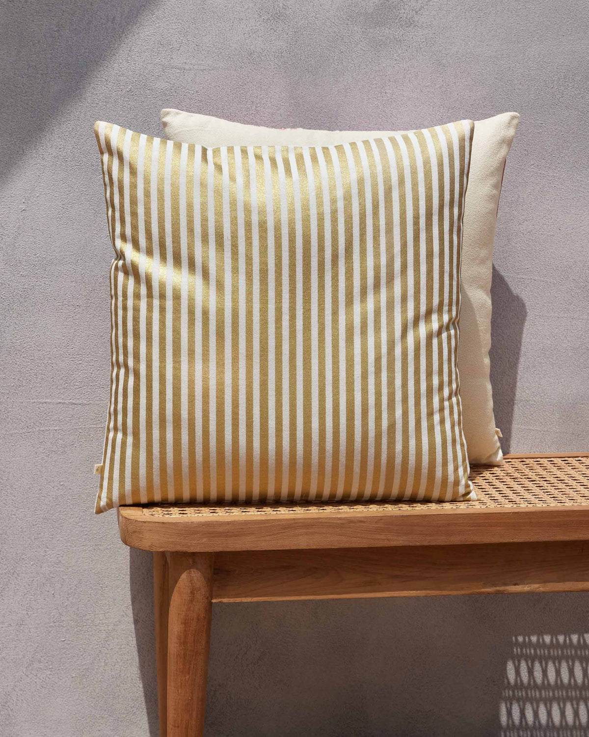 Gold and cream striped cushion on a bench, with a cream cushion behind it.