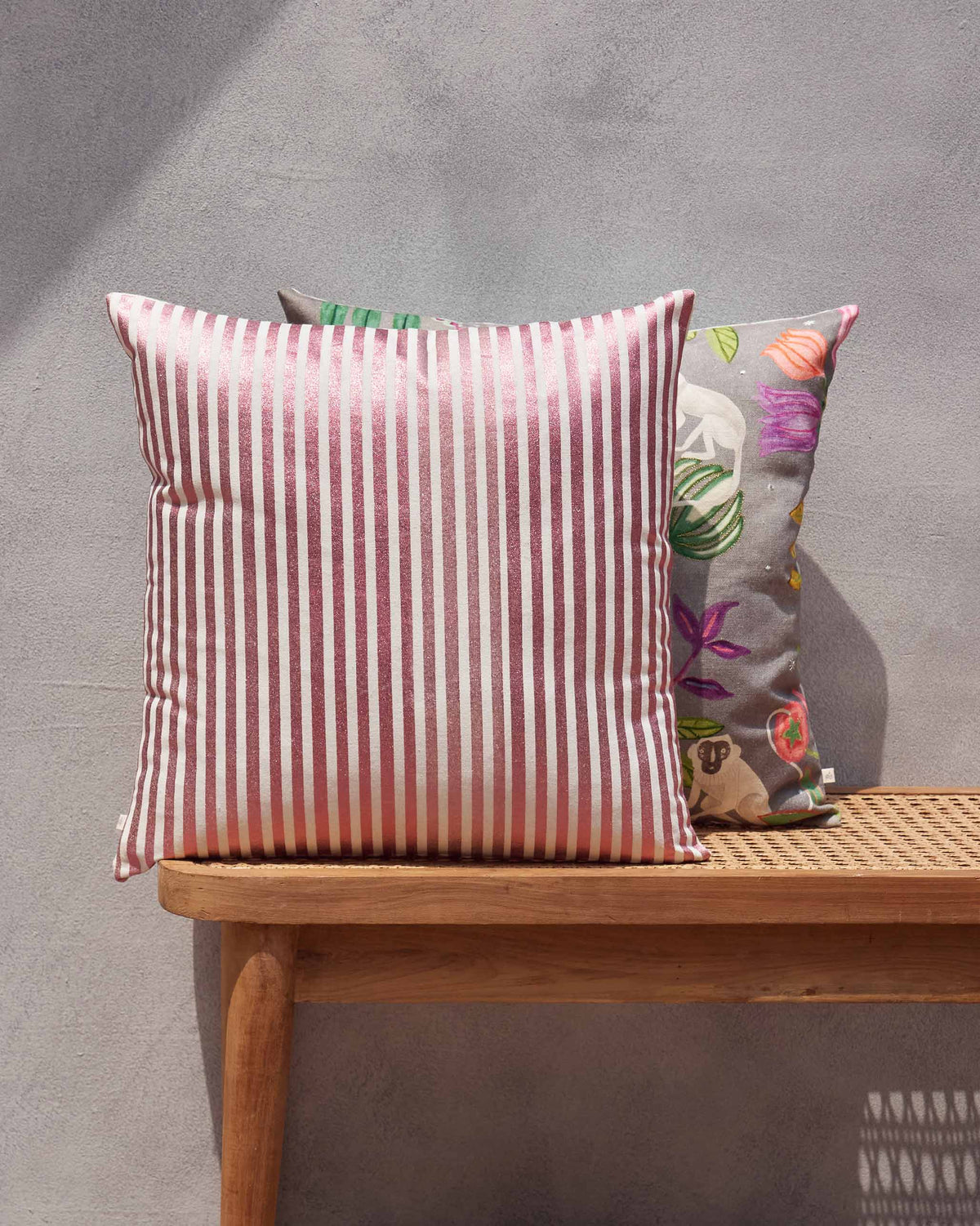 Red striped cushion on a wooden bench beside a grey patterned cushion.