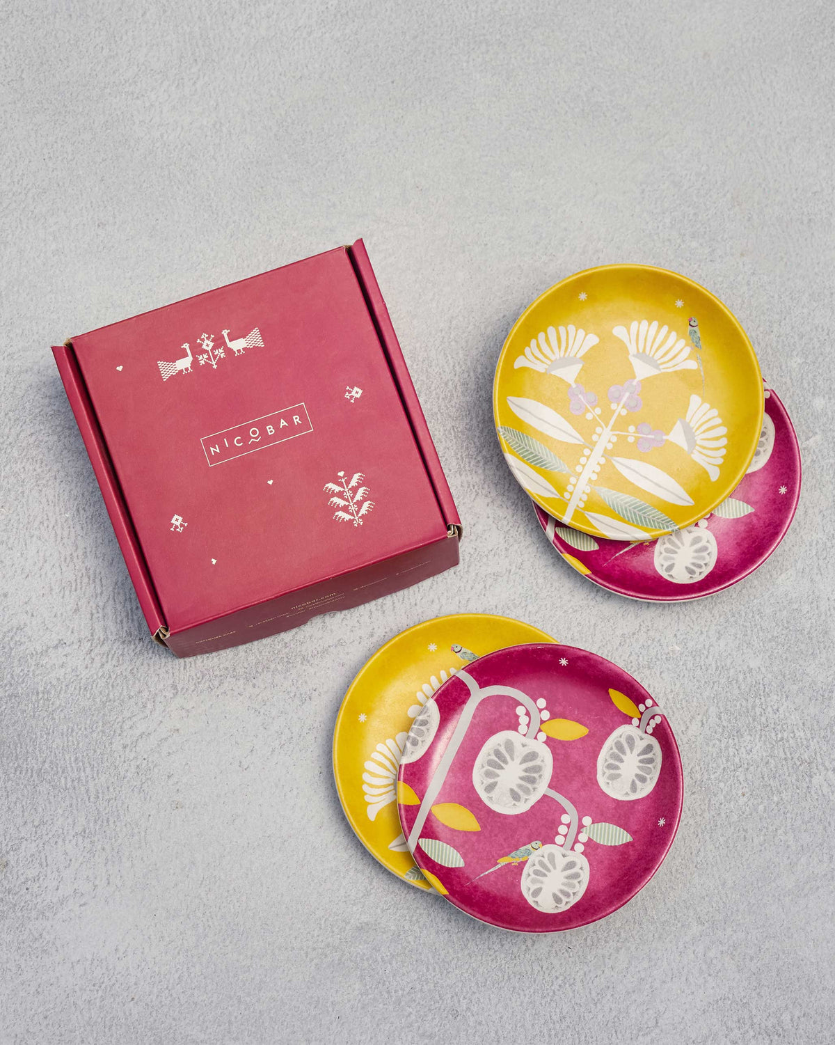 Bahari tea plates fanned out beside a closed red gift box.